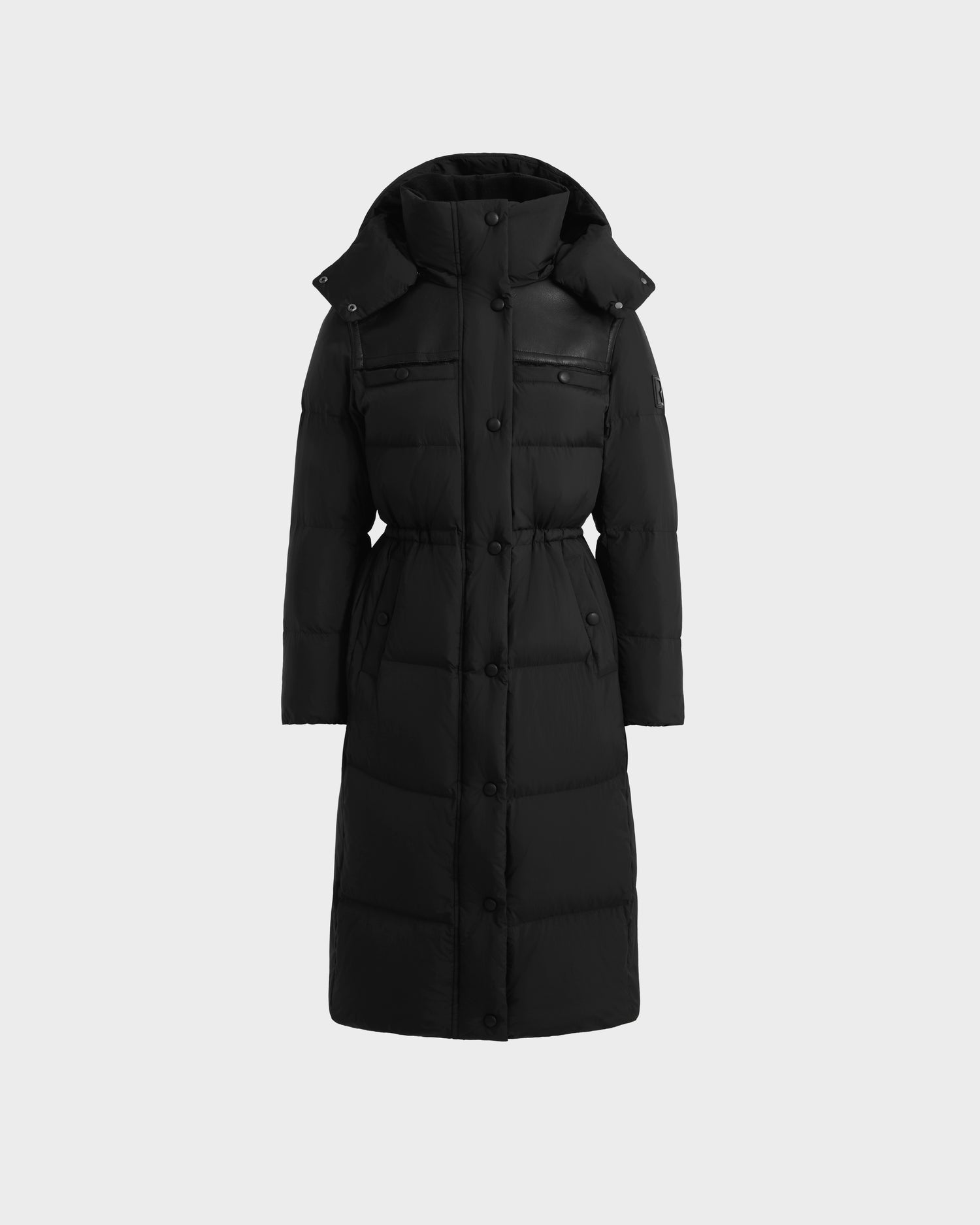 The Rudsak EMBER M-L - L125543 Black women’s long down puffer coat features a removable hood, front button closure, two zippered chest pockets, and a fitted waist, shown against a plain light gray background.