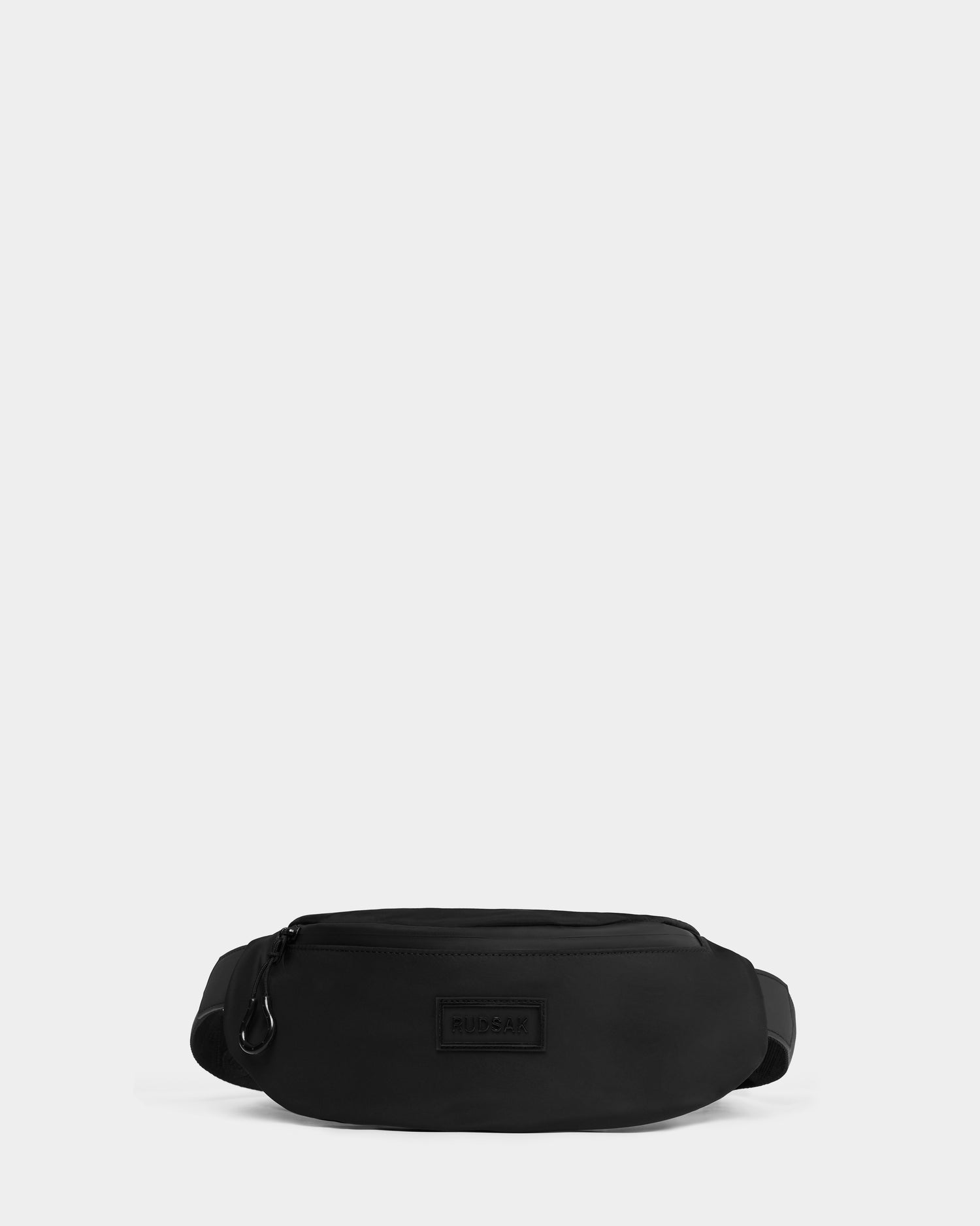 The Rudsak RILO - 9326000 Black waist bag features a zippered main compartment, adjustable strap, and a subtle front logo patch, displayed against a plain light gray background.
