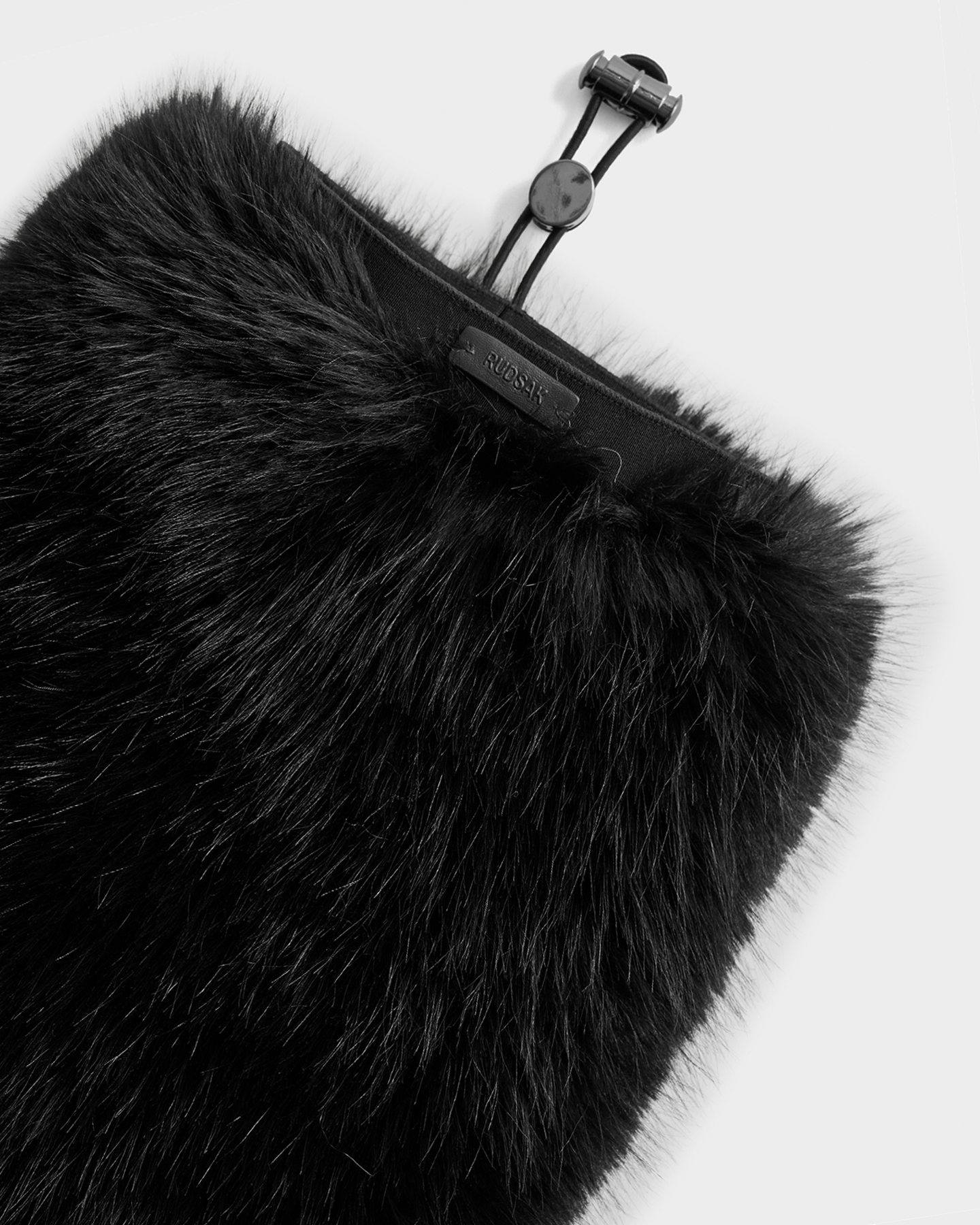 A close-up of the PAIGE - 8425534 Black faux fur bag by Rudsak, featuring a drawstring closure and a small black label near the opening—an après-ski chic winter accessory set against a plain white background.