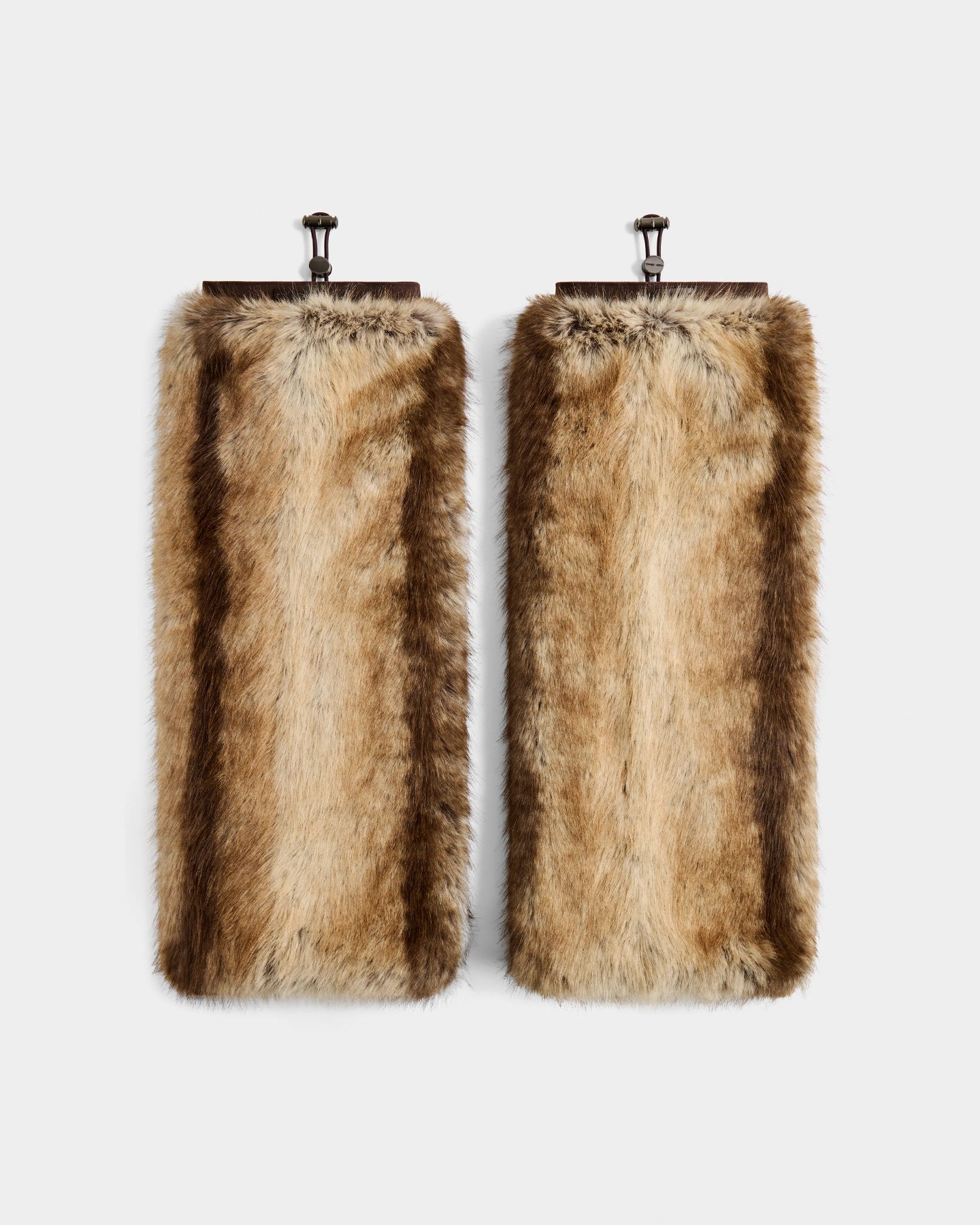 Two rectangular panels display Rudsak's PAIGE - 8425534 Mix Mocha leg warmers in light brown faux fur with dark stripes, hanging from metal hooks—an ideal women’s winter accessory for après-ski chic.