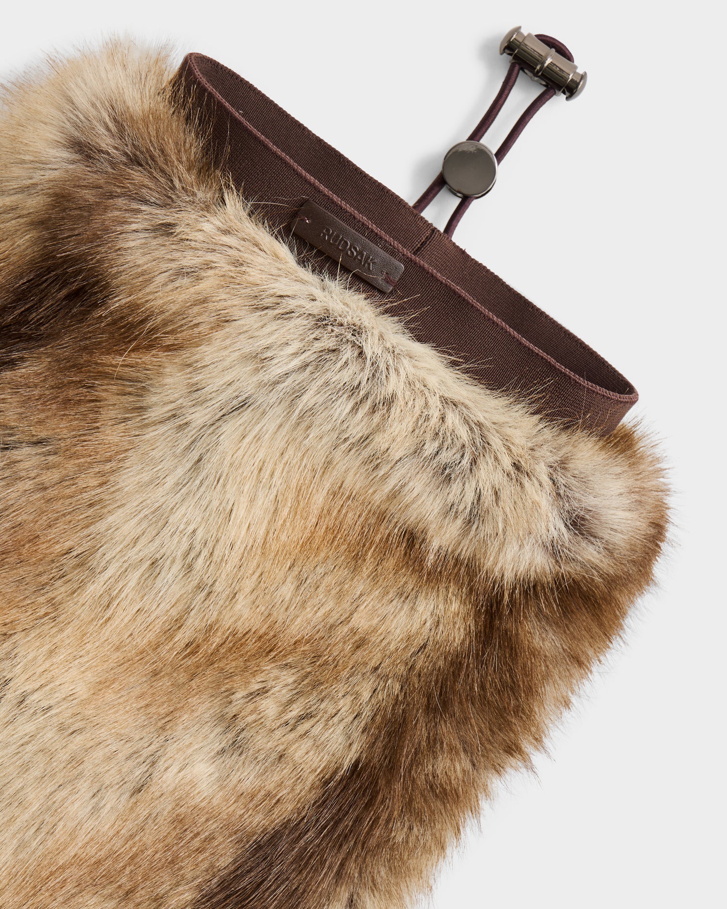A close-up of Rudsak's PAIGE - 8425534 Mix Mocha: a brown and beige faux fur scarf with a dark brown adjustable strap and an interior label, perfect for an après-ski chic style.