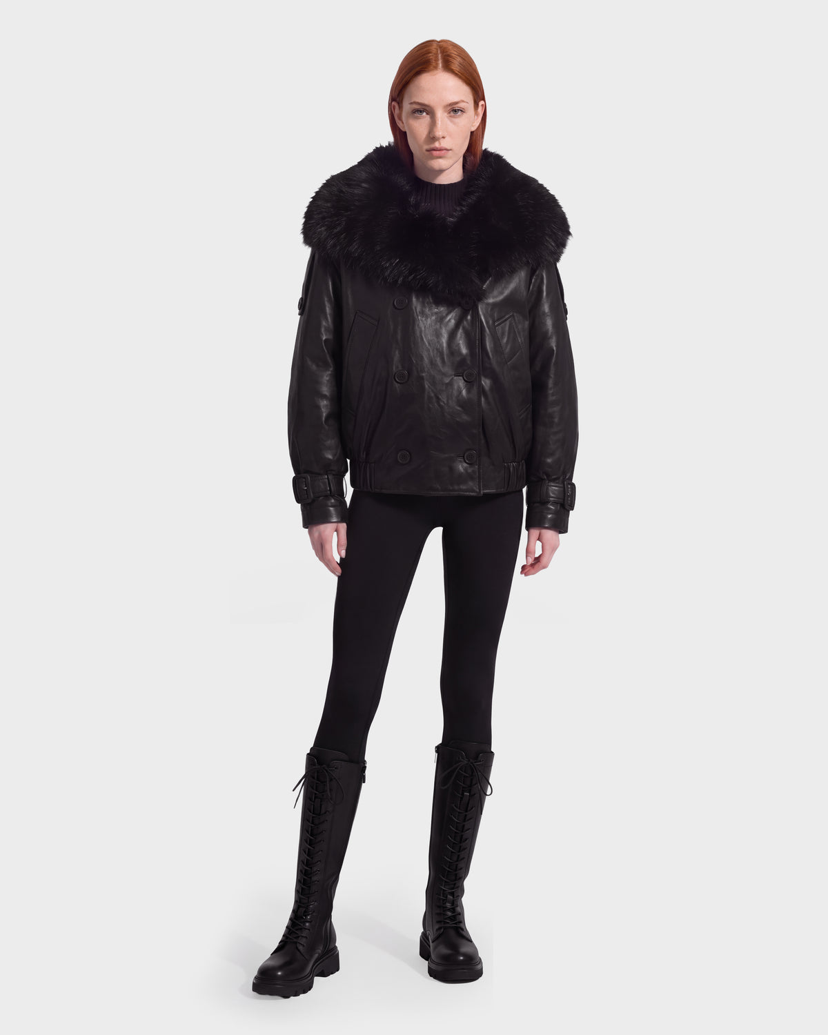 A model wears a Rudsak JANELLE - 8126936 Black double-breasted bomber with a faux fur-trimmed collar, black leggings, and black lace-up knee-high boots.