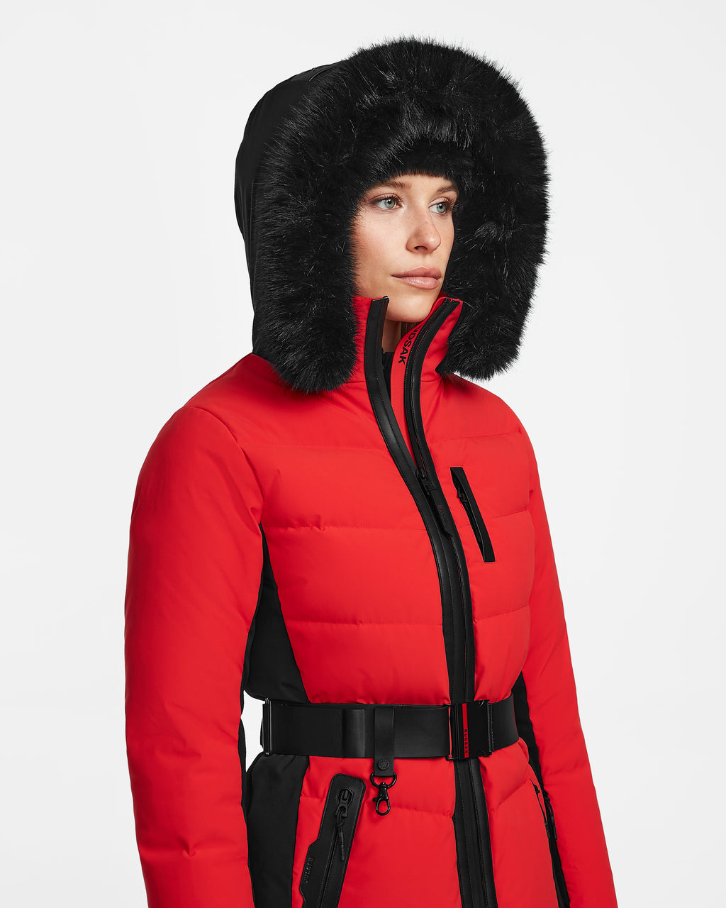 A person wears the Rudsak ALAIA - 8124816 Flame Red fitted ski jacket with black accents, a black faux fur-lined hood, and a black belt, standing against a plain white background.