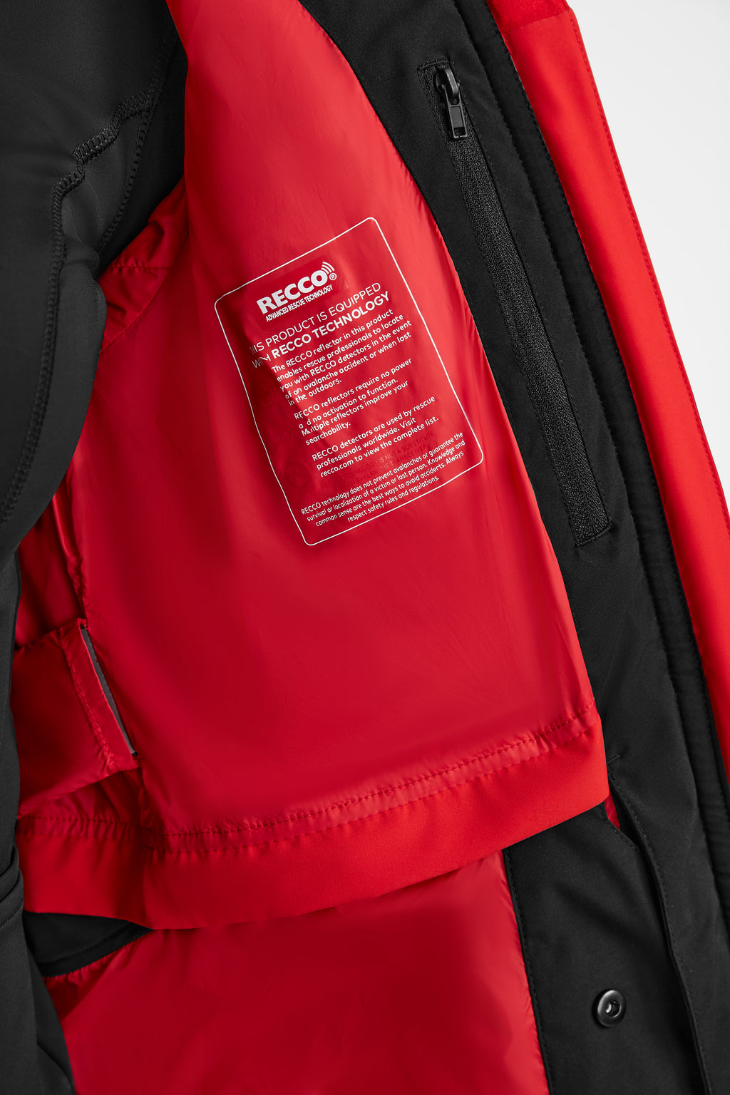 Close-up of the inside of the Rudsak ALAIA - 8124816 Flame Red womens quilted ski jacket, featuring a rectangular red RECCO technology tag sewn onto the red inner lining next to a black zippered pocket.