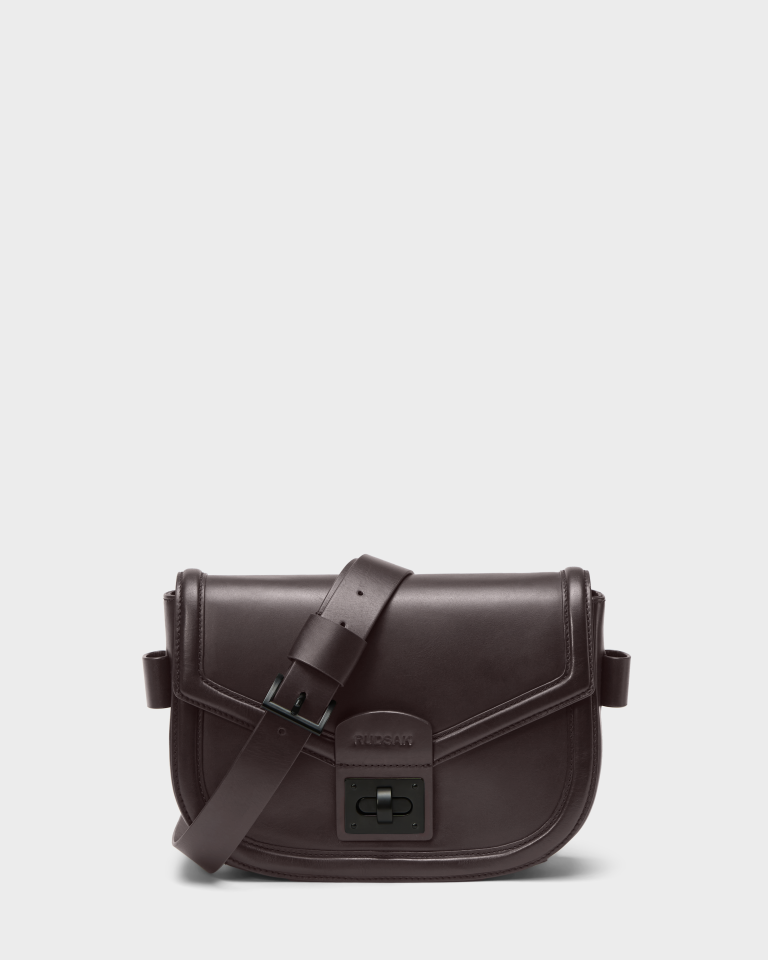 The Rudsak ALORA - 8324506 Bordeaux is a women's leather crossbody bag with a wide adjustable strap, front flap, and rectangular clasp, shown against a plain light gray background.