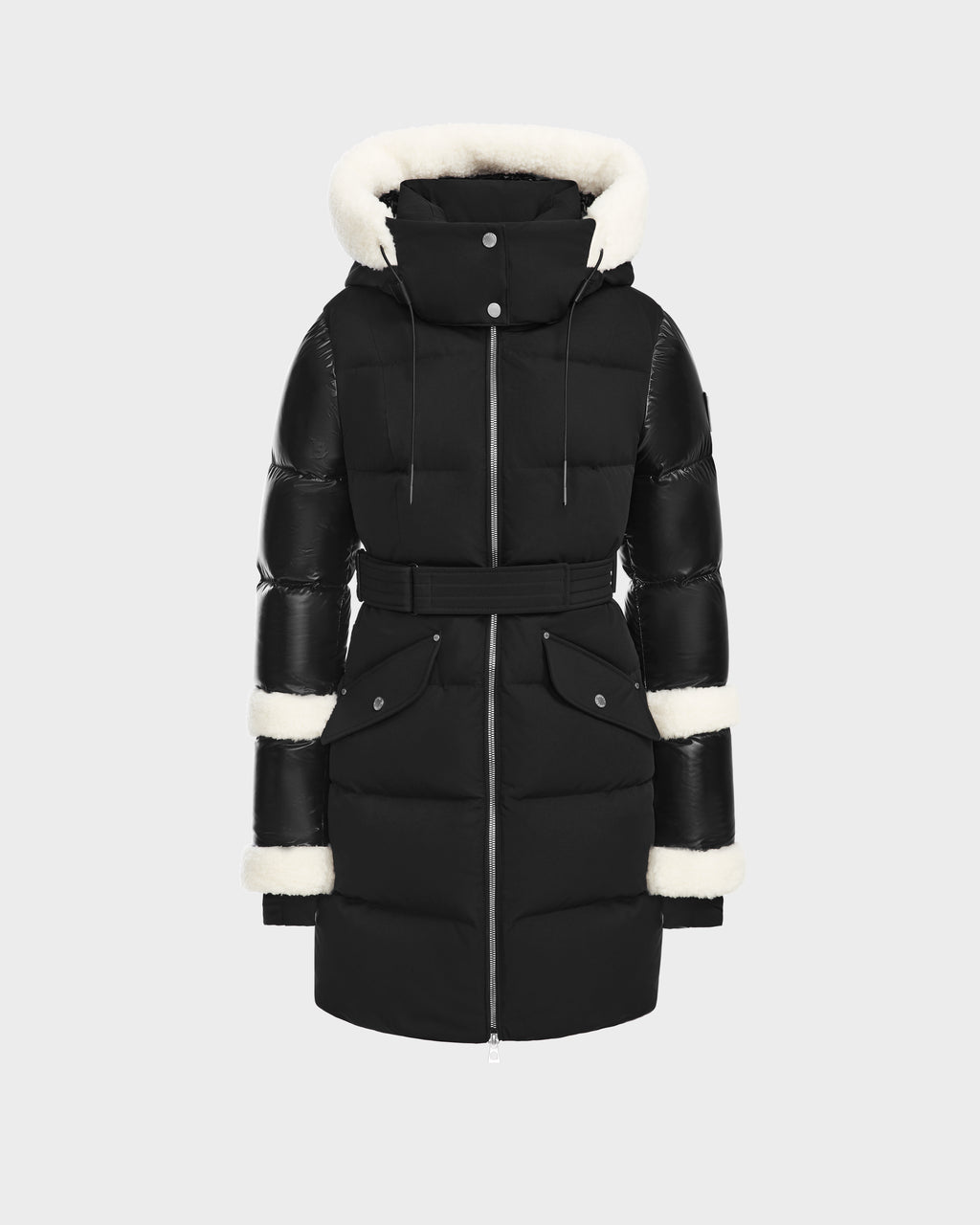 The Rudsak AUDREY L - 8124585 Black/Iceland is a black, knee-length down puffer jacket with a belted waist, two front pockets, and a hood lined with white faux fur. Made from recycled Stormshell fabric and RDS certified down. Displayed on a light background.