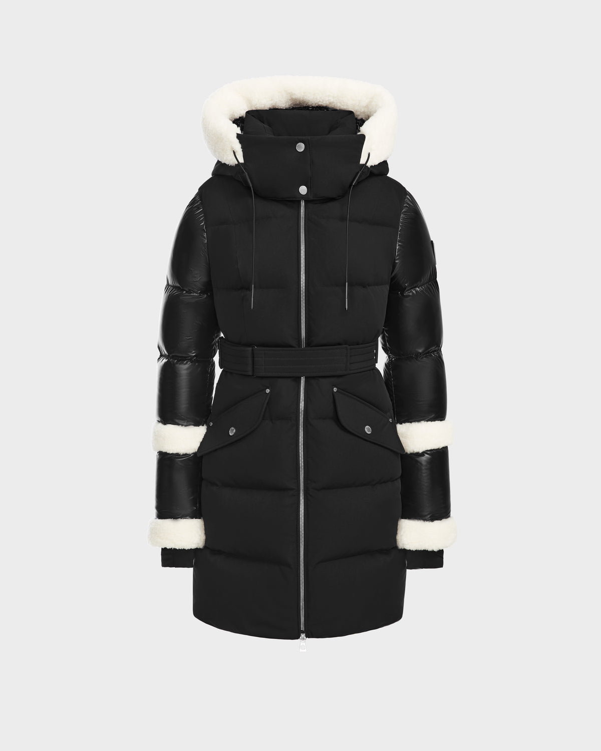 The Rudsak AUDREY L - 8124585 Black/Iceland is a black, knee-length down puffer jacket with a belted waist, two front pockets, and a hood lined with white faux fur. Made from recycled Stormshell fabric and RDS certified down. Displayed on a light background.