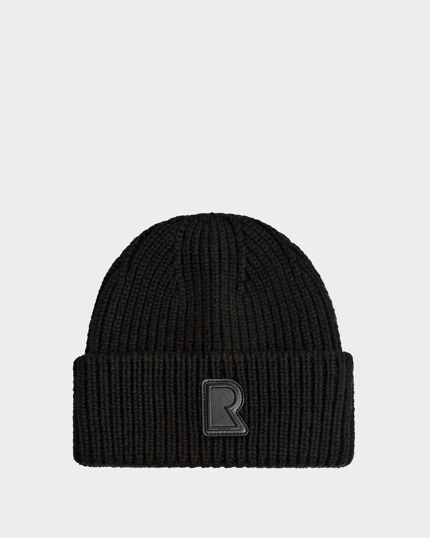 The CYBELLE - 9424504 Black by Rudsak is a unisex black ribbed wool blend beanie with a folded brim and raised R logo patch on the front center, perfect as a stylish winter accessory against a light gray background.