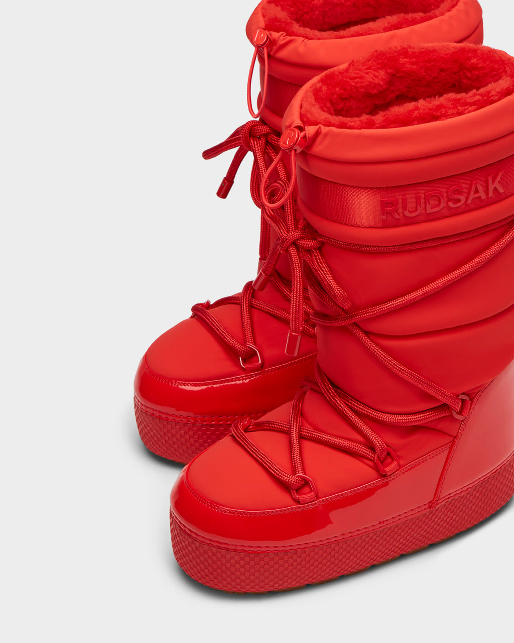 The FARAH - 8223501 Flame Red by Rudsak are shiny, textured women’s winter boots with thick soles, crisscrossed laces, plush lining, and water-repellent finish. The brand is embossed near the top.
