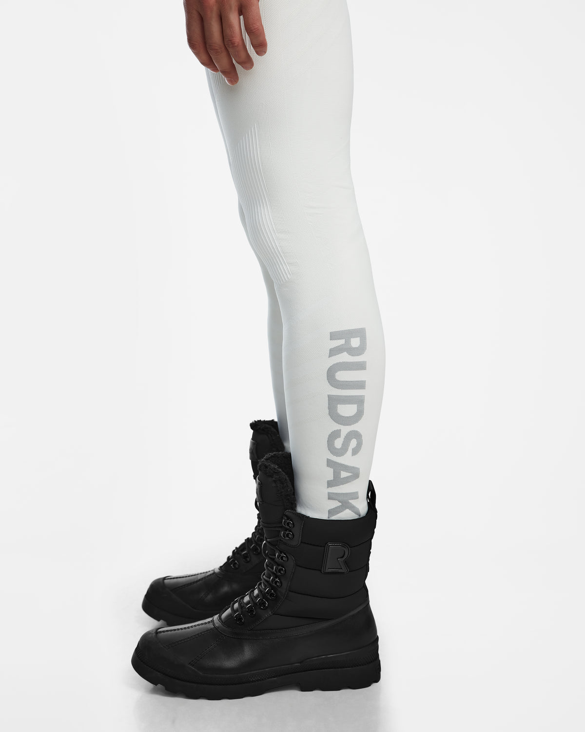 A person wearing the Rudsak FRANC - 6524541 Iceland white stretch underlayer leggings with RUDSAK printed vertically on the side and black lace-up winter boots, standing against a white background.
