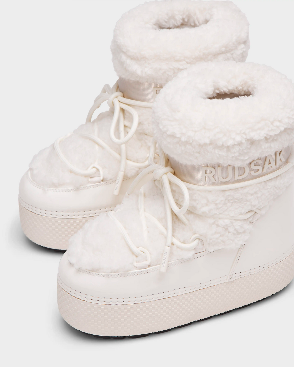 The Rudsak KATHY Y - 1224500 Iceland boots are white, high-top winter boots with thick textured soles, faux fur lining, and laces. Water-repellent and insulated, they feature the Rudsak logo on the side for a cozy, stylish look.