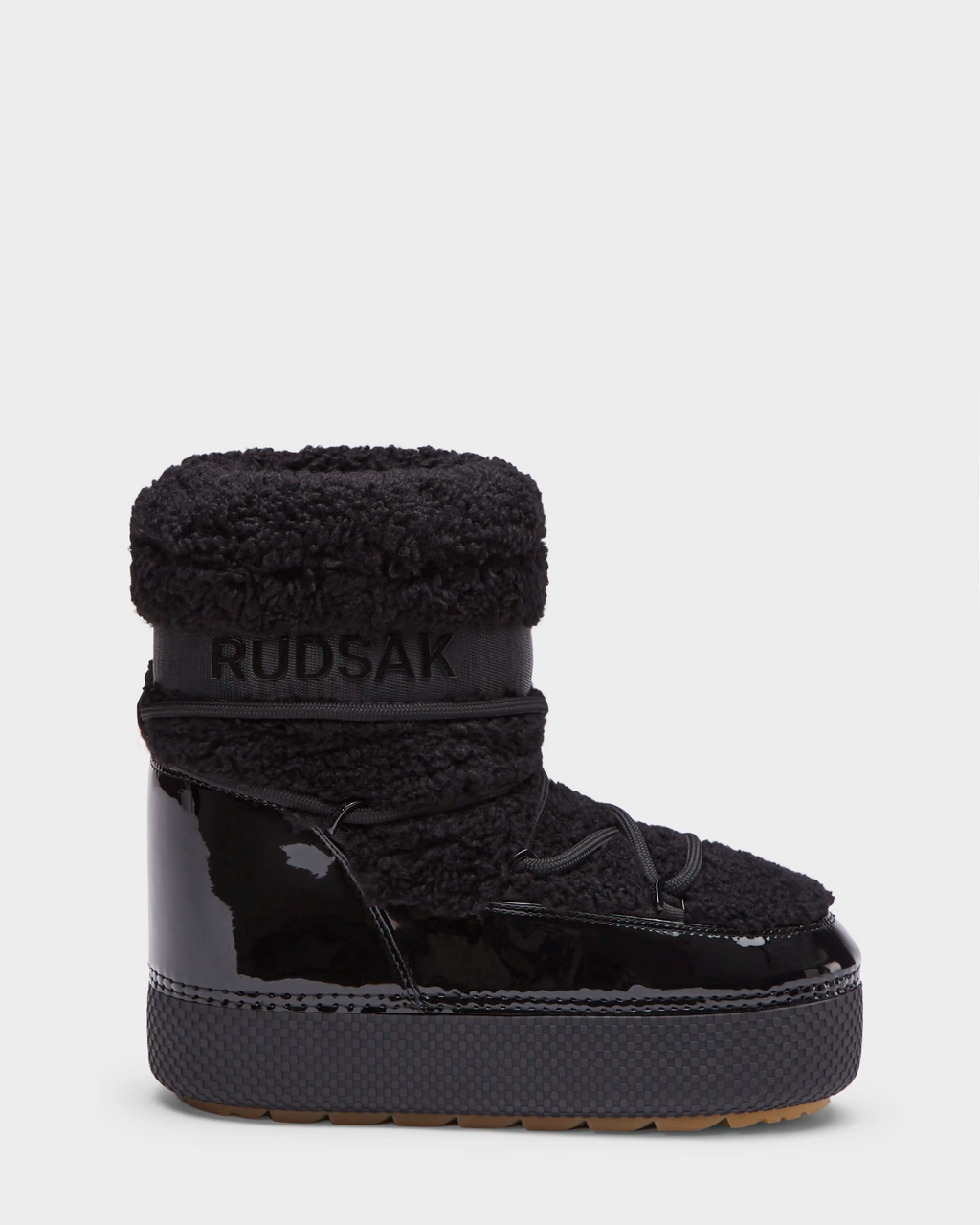 The KATHY - 8223513 Black by Rudsak is a womens winter boot with a shiny, water-repellent patent lower, faux shearling upper, thick treaded sole, and Rudsak branding on the ankle band, shown against a plain white background.
