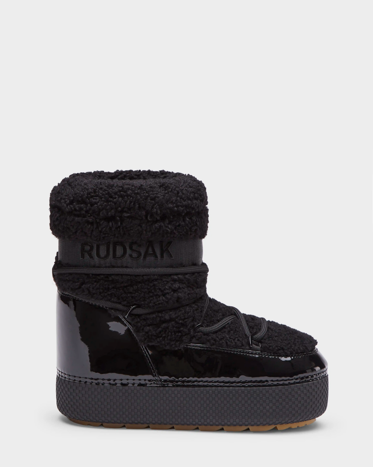 The KATHY - 8223513 Black by Rudsak is a womens winter boot with a shiny, water-repellent patent lower, faux shearling upper, thick treaded sole, and Rudsak branding on the ankle band, shown against a plain white background.