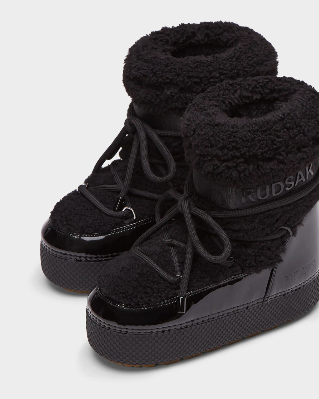 The KATHY - 8223513 Black by Rudsak is a womens winter boot with glossy lowers, textured platform soles, soft faux shearling uppers, laces, and RUDSAK branding on the ankle.