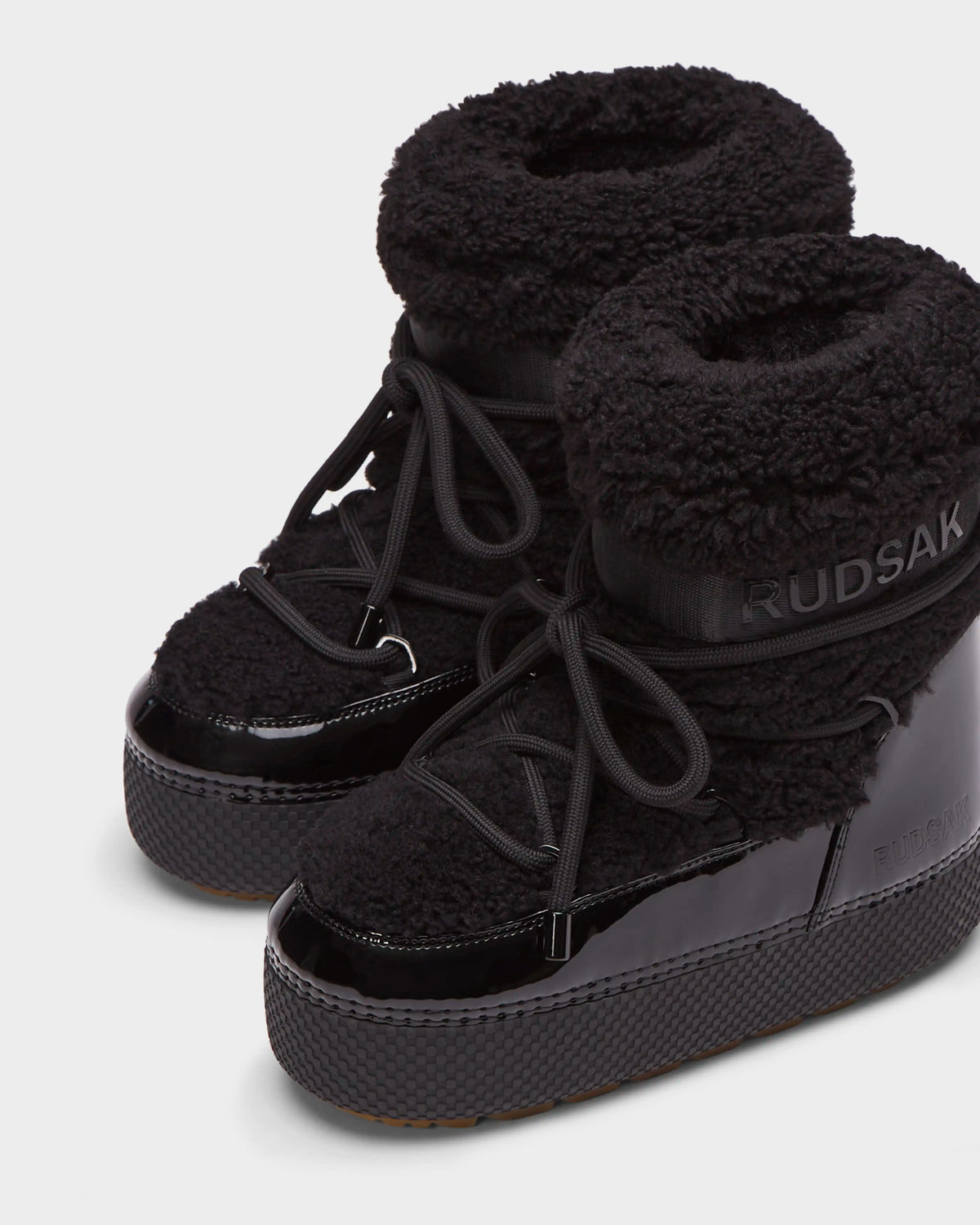The KATHY - 8223513 Black by Rudsak is a womens winter boot with glossy lowers, textured platform soles, soft faux shearling uppers, laces, and RUDSAK branding on the ankle.