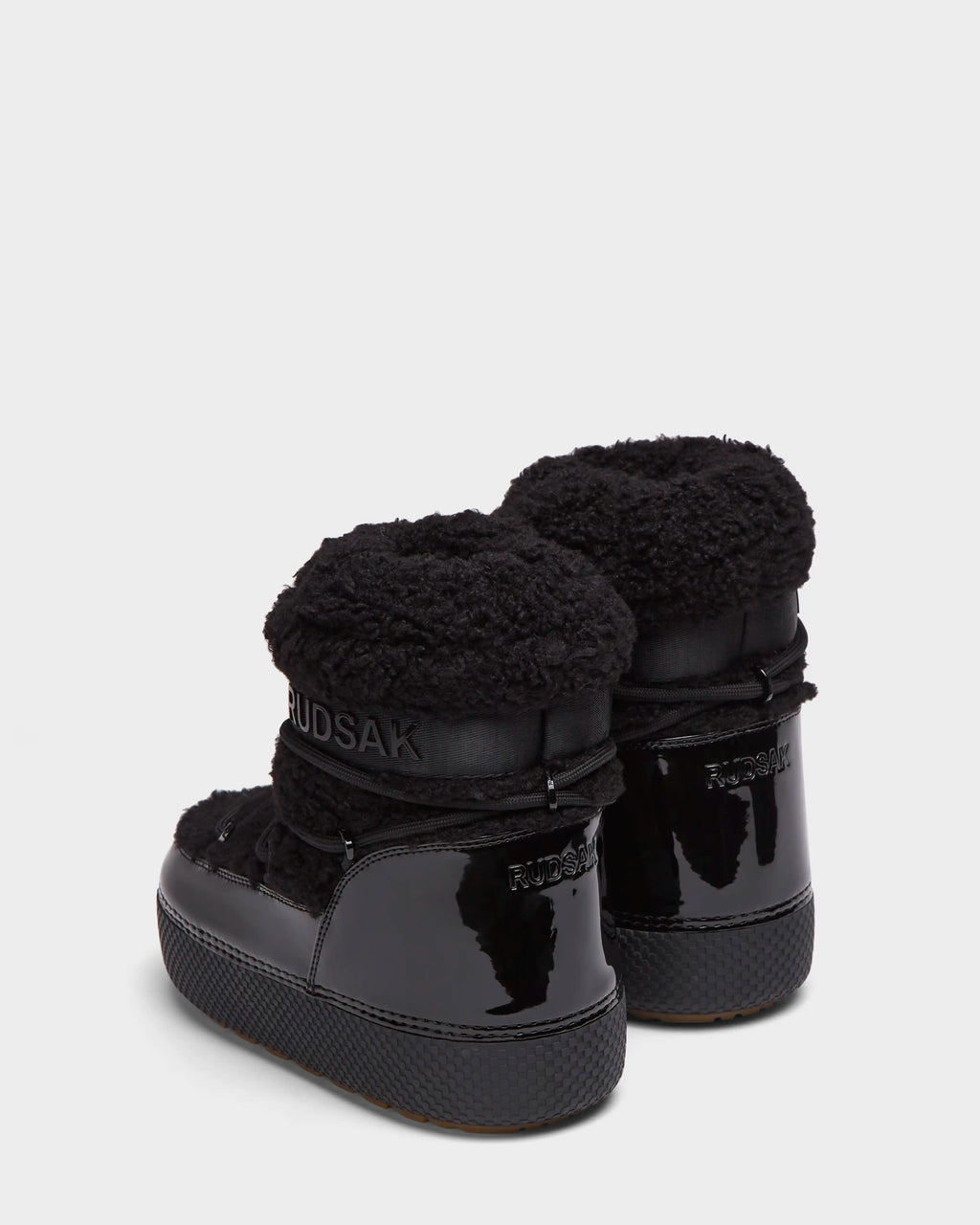 The KATHY - 8223513 Black womens winter boots by Rudsak feature black patent leather, textured rubber soles, and plush cuffs with the Rudsak logo. Shown from the back on a white background, these water-repellent boots highlight stylish design.