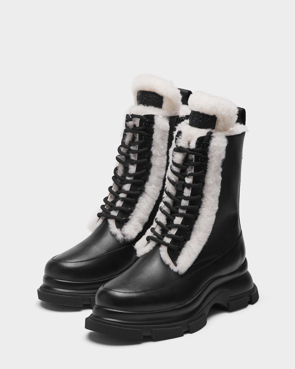 The Rudsak LANA S - 8224537 Black boots feature chunky soles, black mid-calf lace-up design, and visible white shearling lining at the tongue and sides, set against a plain light background.