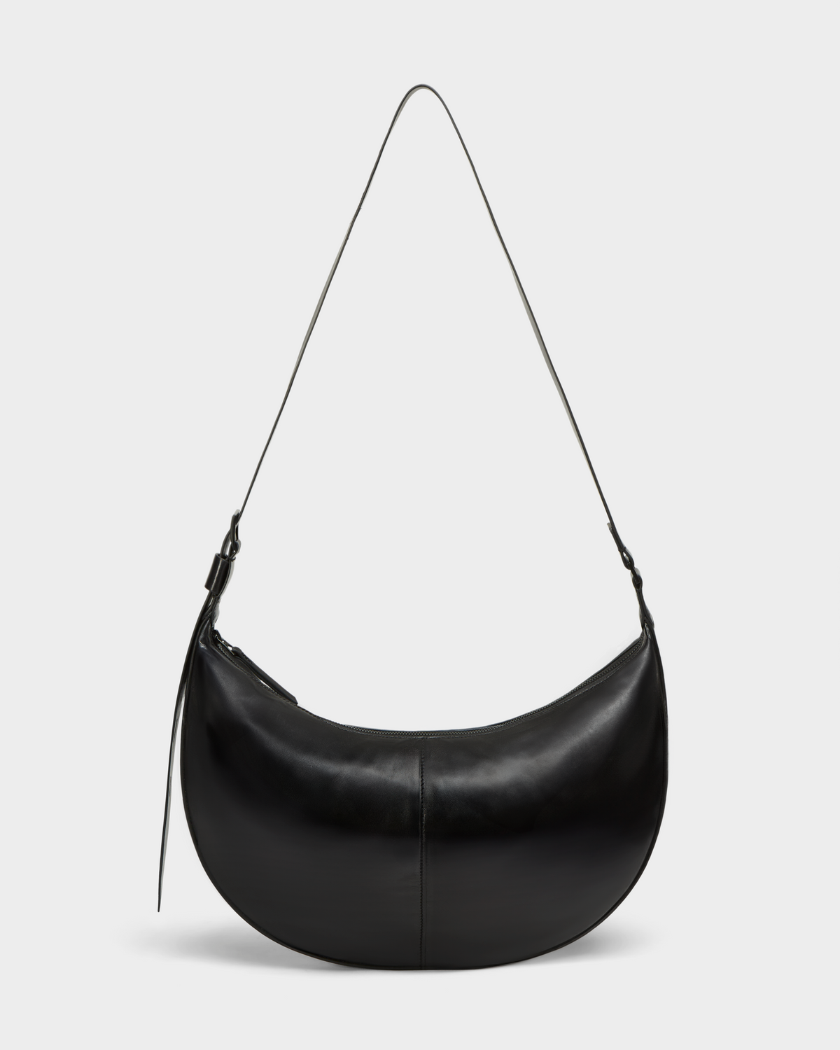 The LANISSA - 8324505 Black by Rudsak is a black crescent-shaped womens leather bag with a long, thin strap and minimalist design, shown against a plain light gray background.