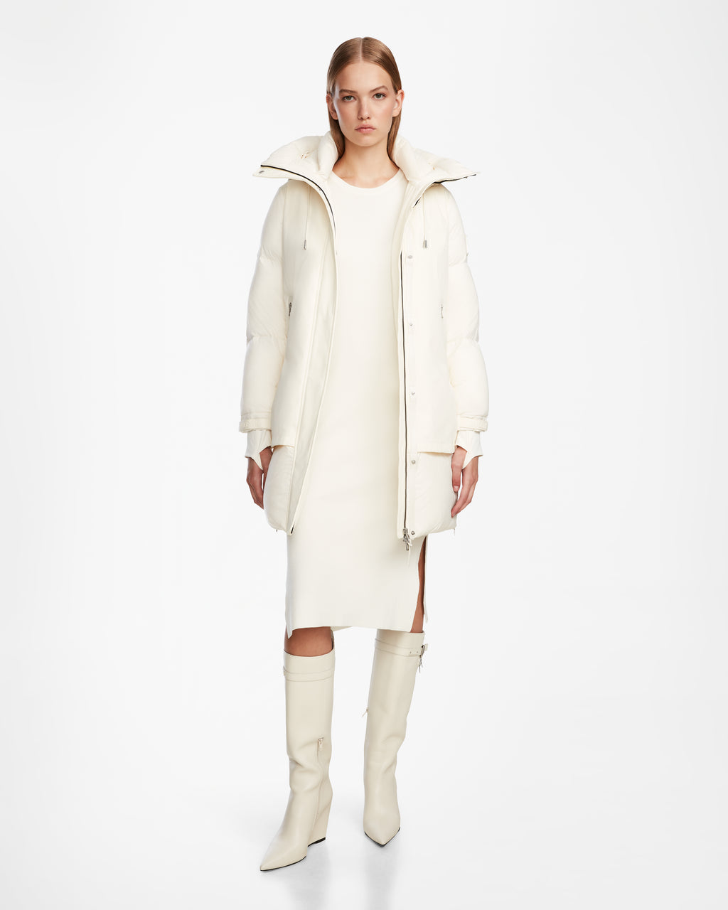 A woman stands against a white background wearing the Rudsak LAYAN - 8124576 Iceland long off-white winter coat, paired with a matching knee-length dress and knee-high heeled boots.