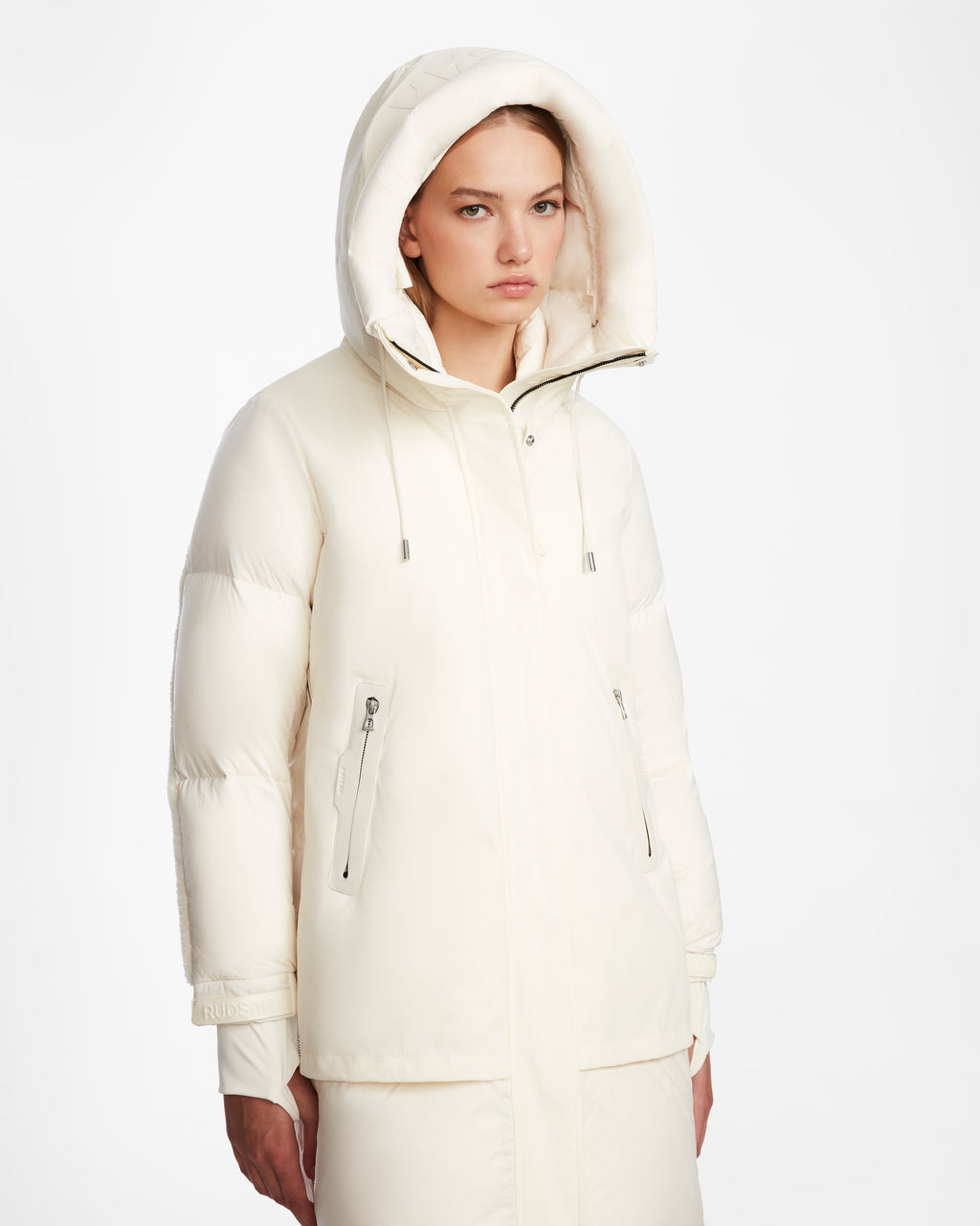 A woman wears the Rudsak LAYAN - 8124576 Iceland white womens down parka with zippered pockets, standing against a plain white background and looking forward with a neutral expression.