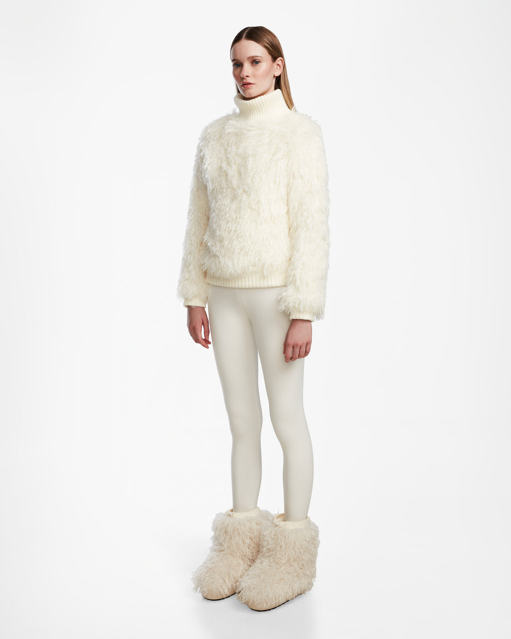 A woman with straight, long hair and a neutral expression wears the Rudsak LAYLA M - 8524600 Iceland faux Mongolian fur turtleneck, matching white leggings, and oversized cream boots against a white background in après-ski style.