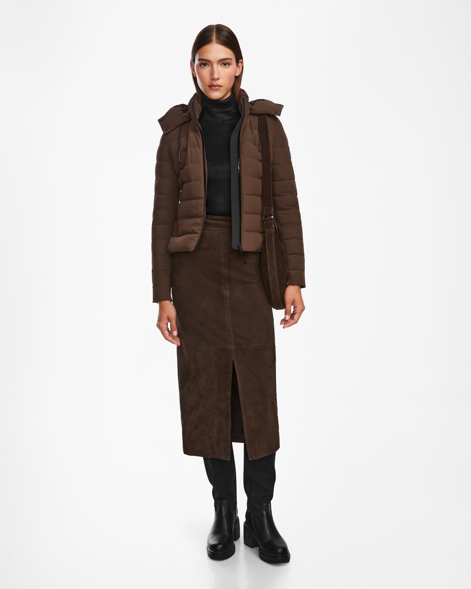A woman faces forward in the Rudsak MELISSA - 8124824 Espresso lightweight down puffer jacket, worn with a black turtleneck, brown midi skirt with front slit, black leggings, and black boots against a plain white background.