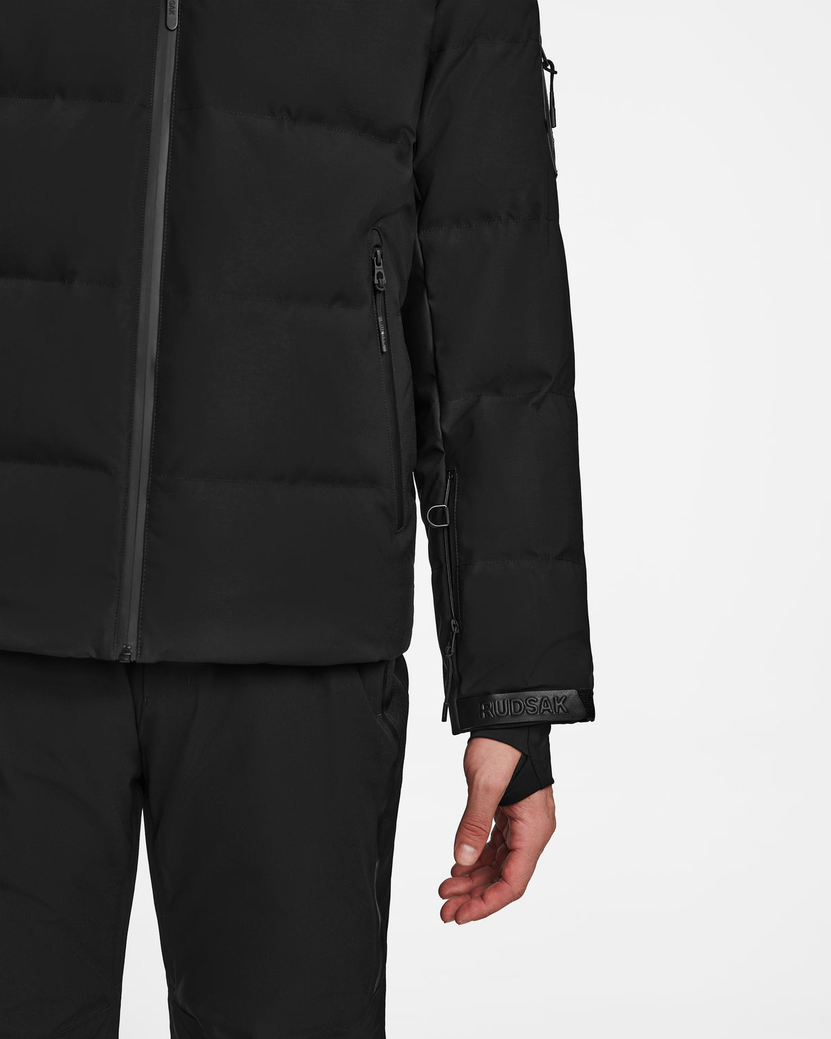 A person wears the Rudsak MICHEL - 6124517 Black down ski jacket and black pants, shown from shoulders to mid-thigh, right arm relaxed at their side, against a plain white background.