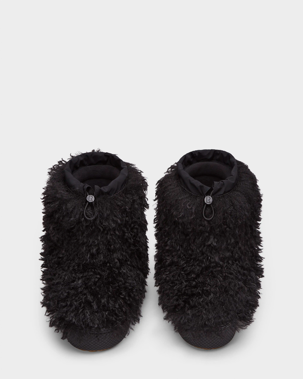 Displayed on a plain white background, the Rudsak ROSSY - 8224518 Black slippers feature black Mongolian fur, textured soles, and adjustable drawstring closures, inspired by women’s slip-on winter boots.