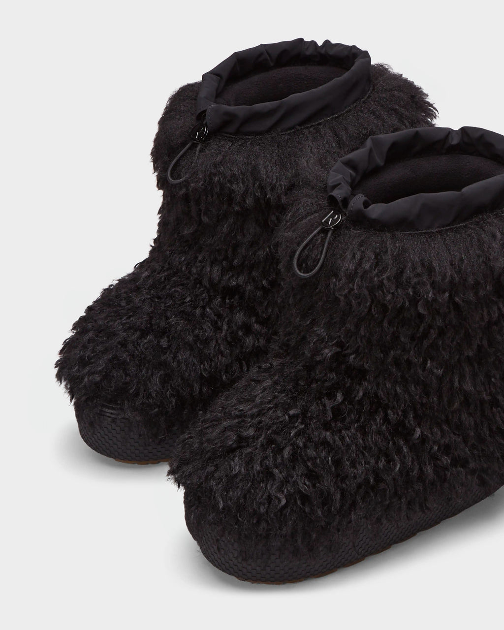 The ROSSY - 8224518 Black by Rudsak are black après-ski slippers crafted from curly Mongolian fur with a textured sole and adjustable drawstring cuffs, shown side by side on a light background.