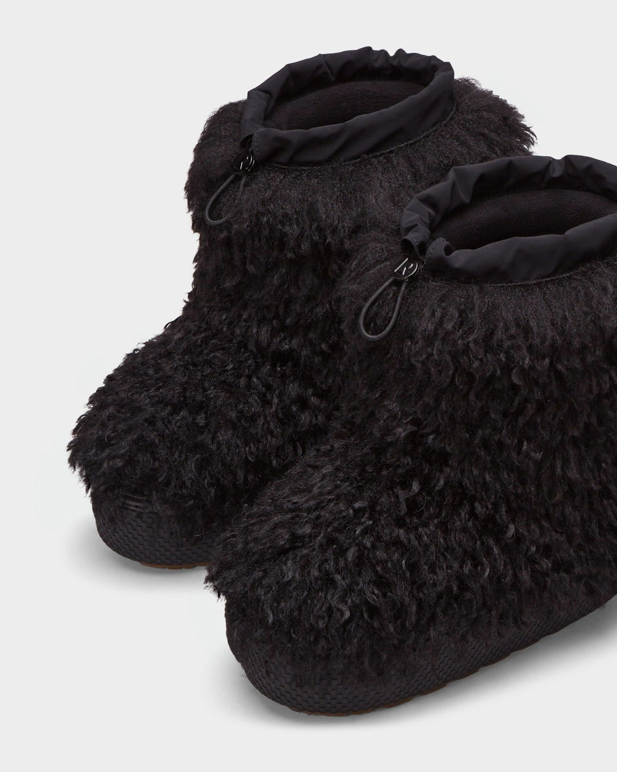 The ROSSY - 8224518 Black by Rudsak are black après-ski slippers crafted from curly Mongolian fur with a textured sole and adjustable drawstring cuffs, shown side by side on a light background.