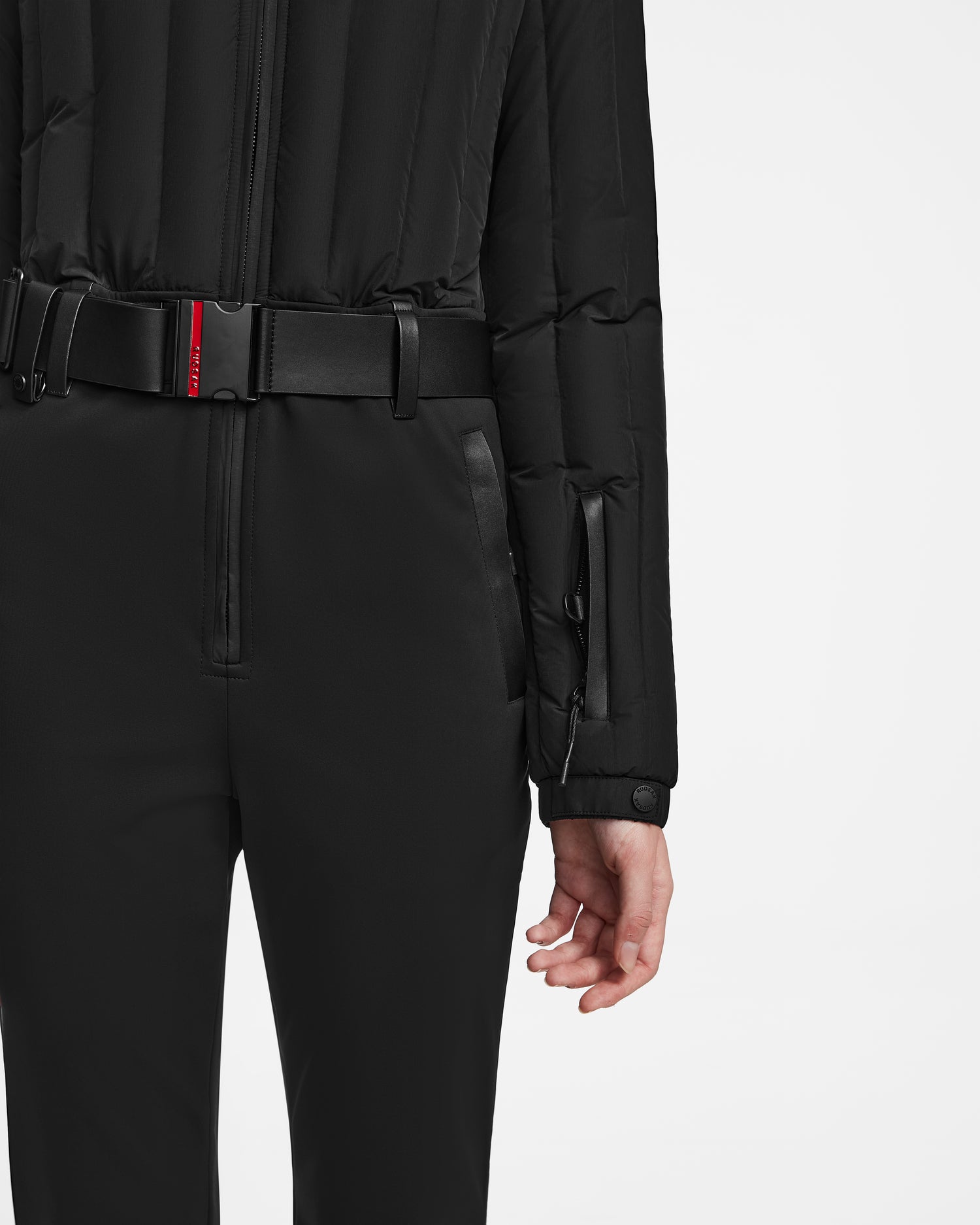 A person shown from the back against a white background wears Rudsak’s SAGE - 8124782 Black quilted jacket with snap button cuffs and RECCO rescue technology, paired with black pants and a black belt featuring a red detail.