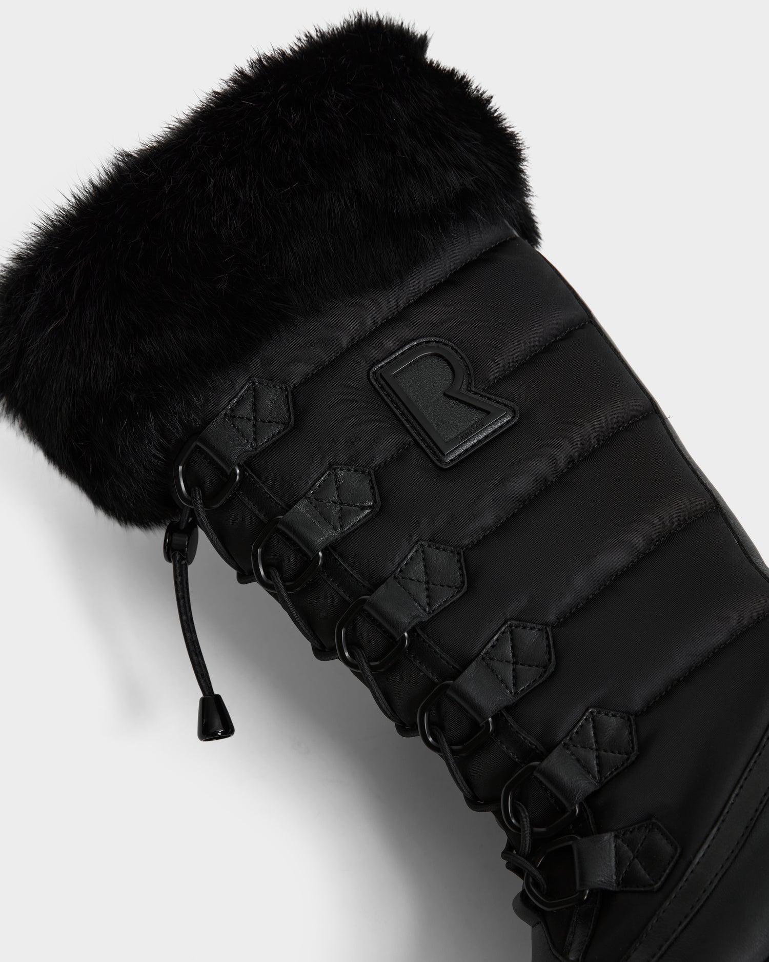 Close-up of the Rudsak WINDY - L224507 Black women’s winter boot, featuring faux fur trim, lace-up detailing, quilted stitching, a raised R logo on the side, and cold-weather comfort design.