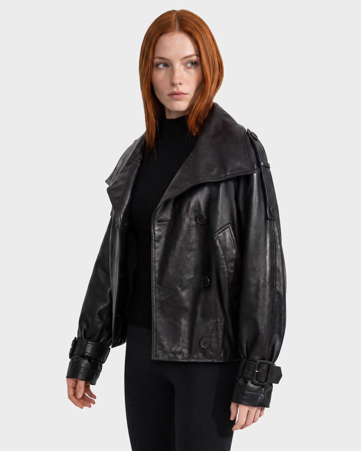 Woman wearing a black Rudsak JANELLE - 8126936 Black double-breasted leather bomber with wide lapels and buckled cuffs over a black ribbed sweater.