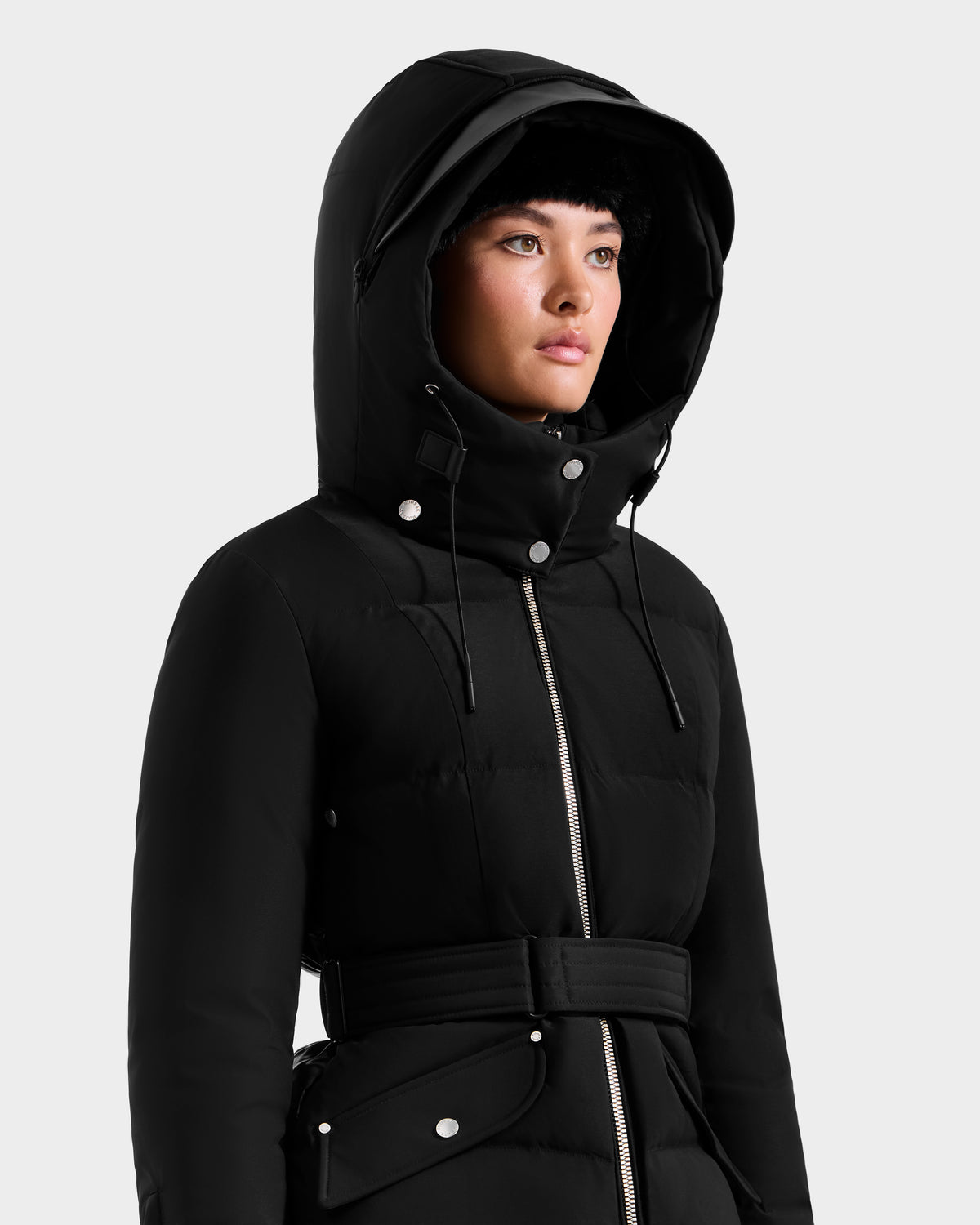 A woman models the Rudsak ADELINE H - 8125587 black jacket with a belted waist and silver buttons, standing against a plain light background to highlight this chic winter coat.