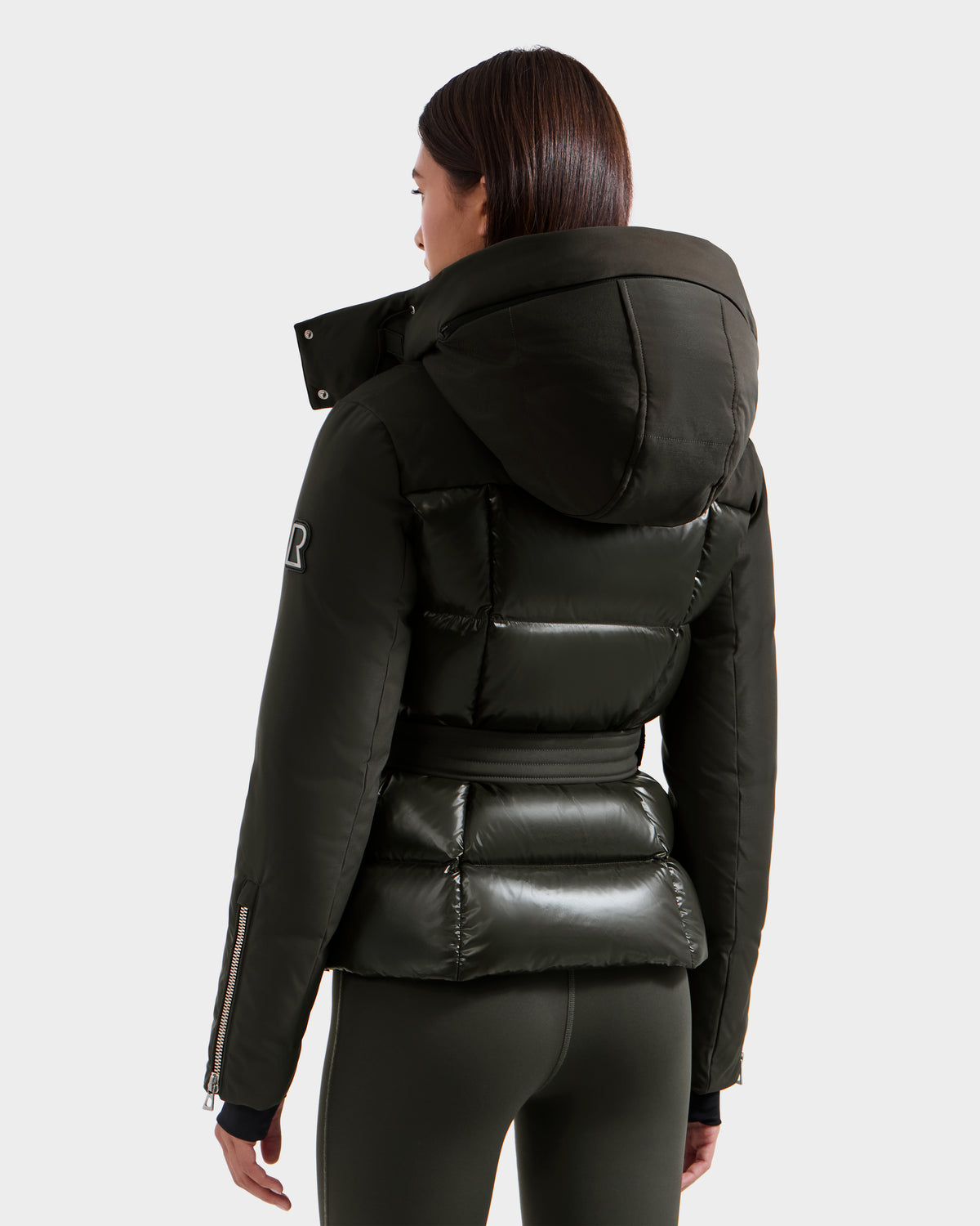 A woman is seen from behind wearing the Rudsak ADELINE H - 8125587 Dark Olive winter jacket with matching leggings, showcasing its quilted sections and fitted puffer-style design.