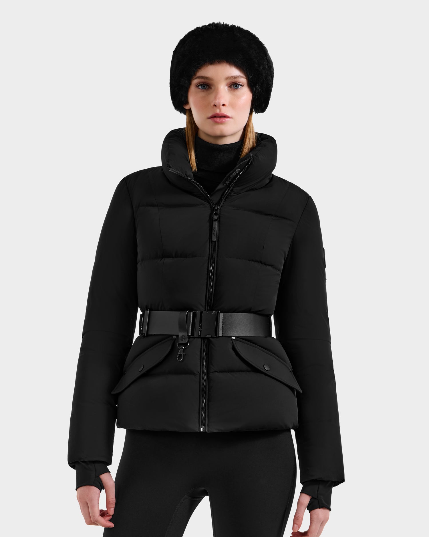 A woman models the Rudsak ADELINE - 8124544 Black belted quilted winter jacket against a plain light gray background, looking directly at the camera.