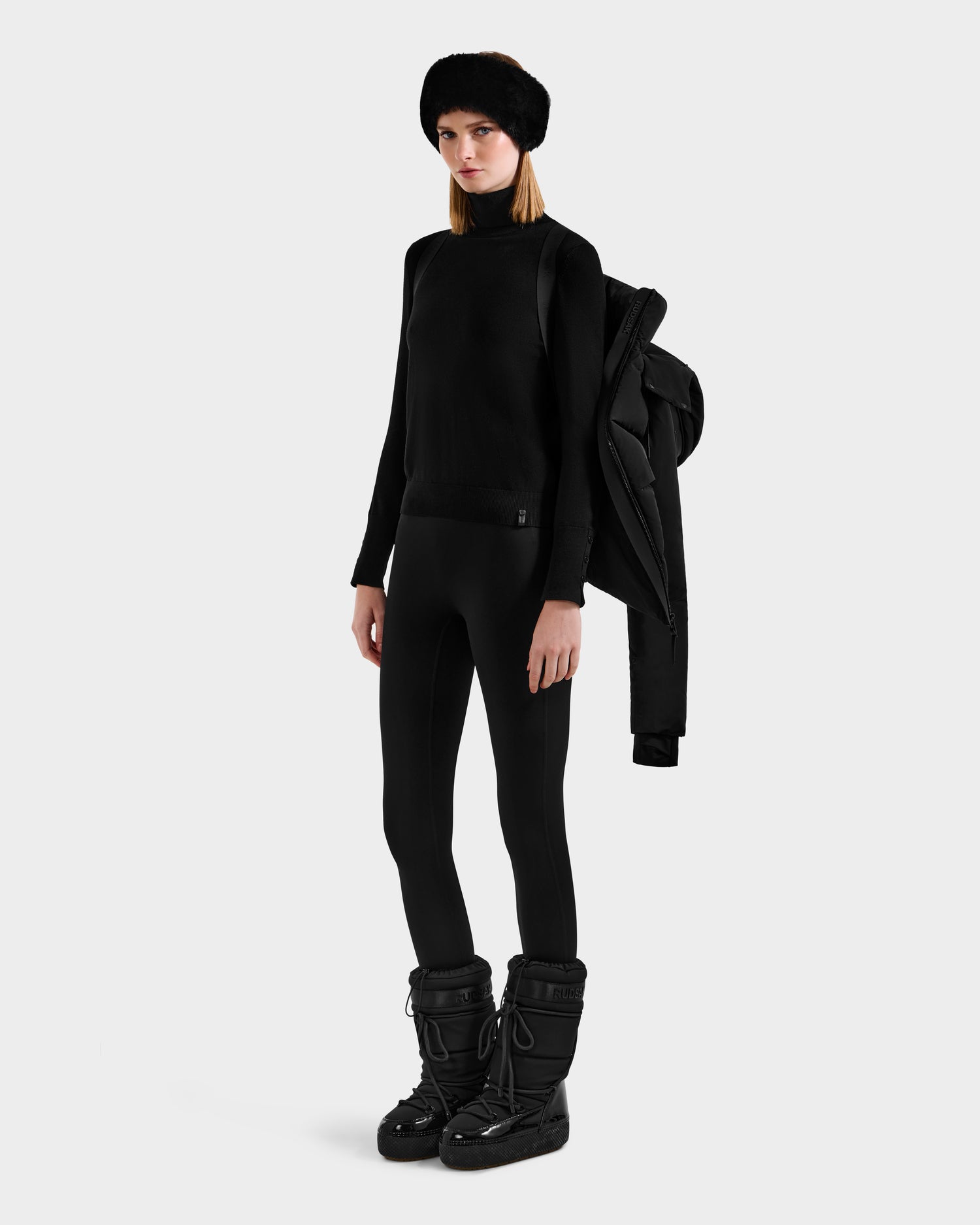 Wearing the Rudsak ADELINE - 8124544 Black women's down puffer draped over one shoulder, a person in black attire poses against a plain light background.