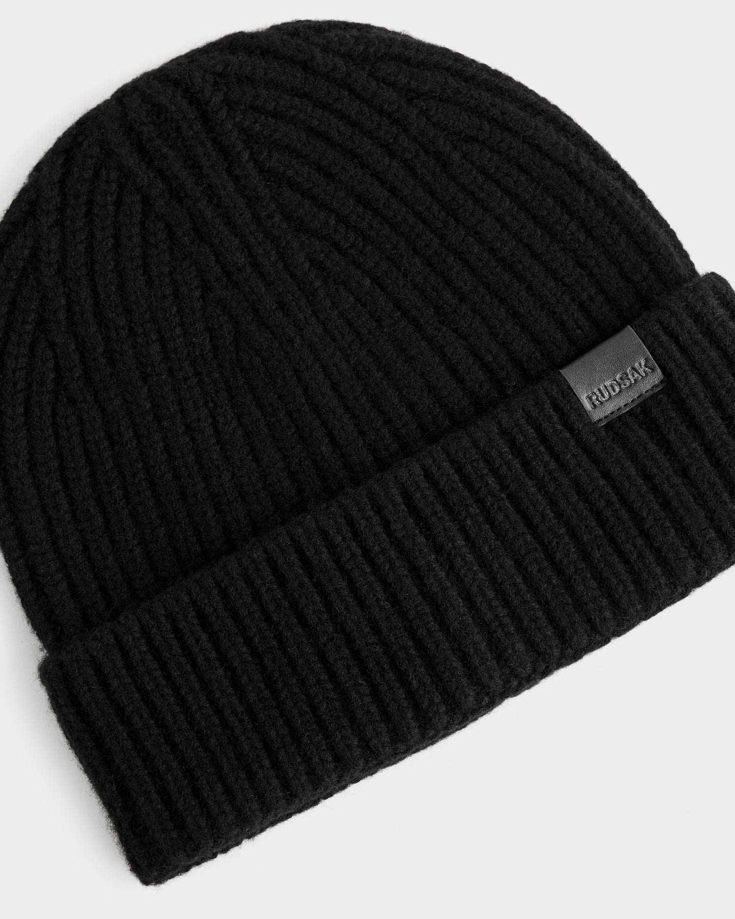 The ALINA - L425540 Black beanie by Rudsak is a women’s ribbed knit winter hat in black wool-cashmere, with a folded brim and a small rectangular Rudsak tag. It is shown against a plain white background.