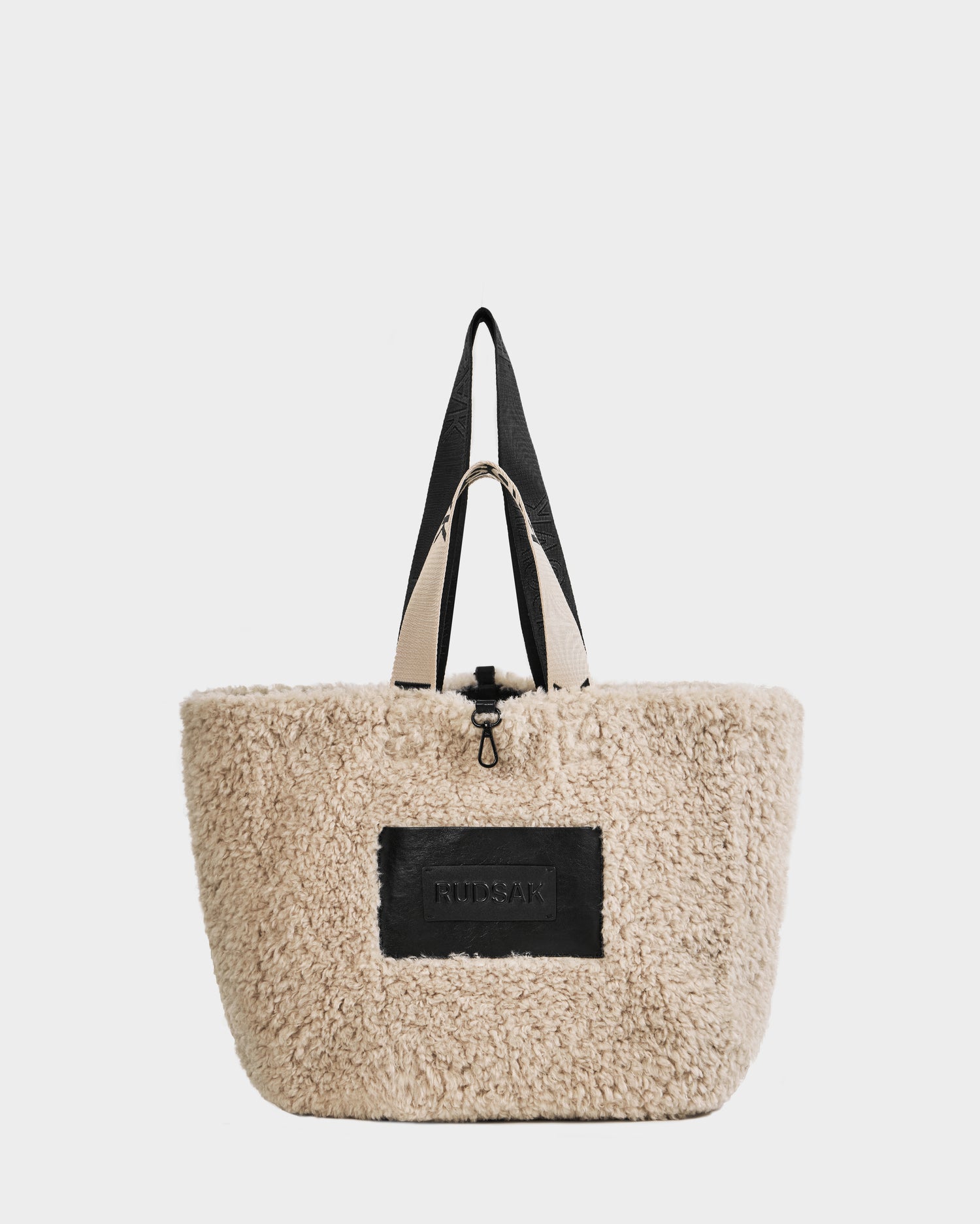 A beige, fluffy faux shearling bag with black handles and a large black patch on the front displaying the brand name Rudsak. The ANNIAH - 8325541 Black bag is photographed against a plain white background.