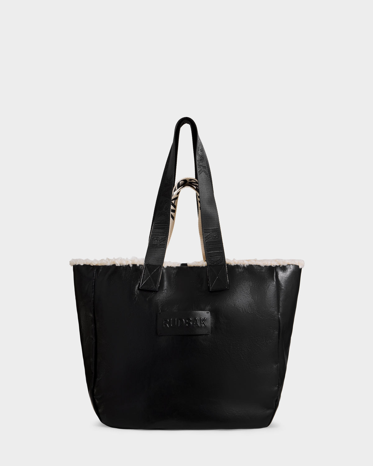 The Rudsak ANNIAH - 8325541 Black/Vanilla is a large reversible tote with double handles, soft white faux shearling trim, and a front patch. Photographed against a plain white background.