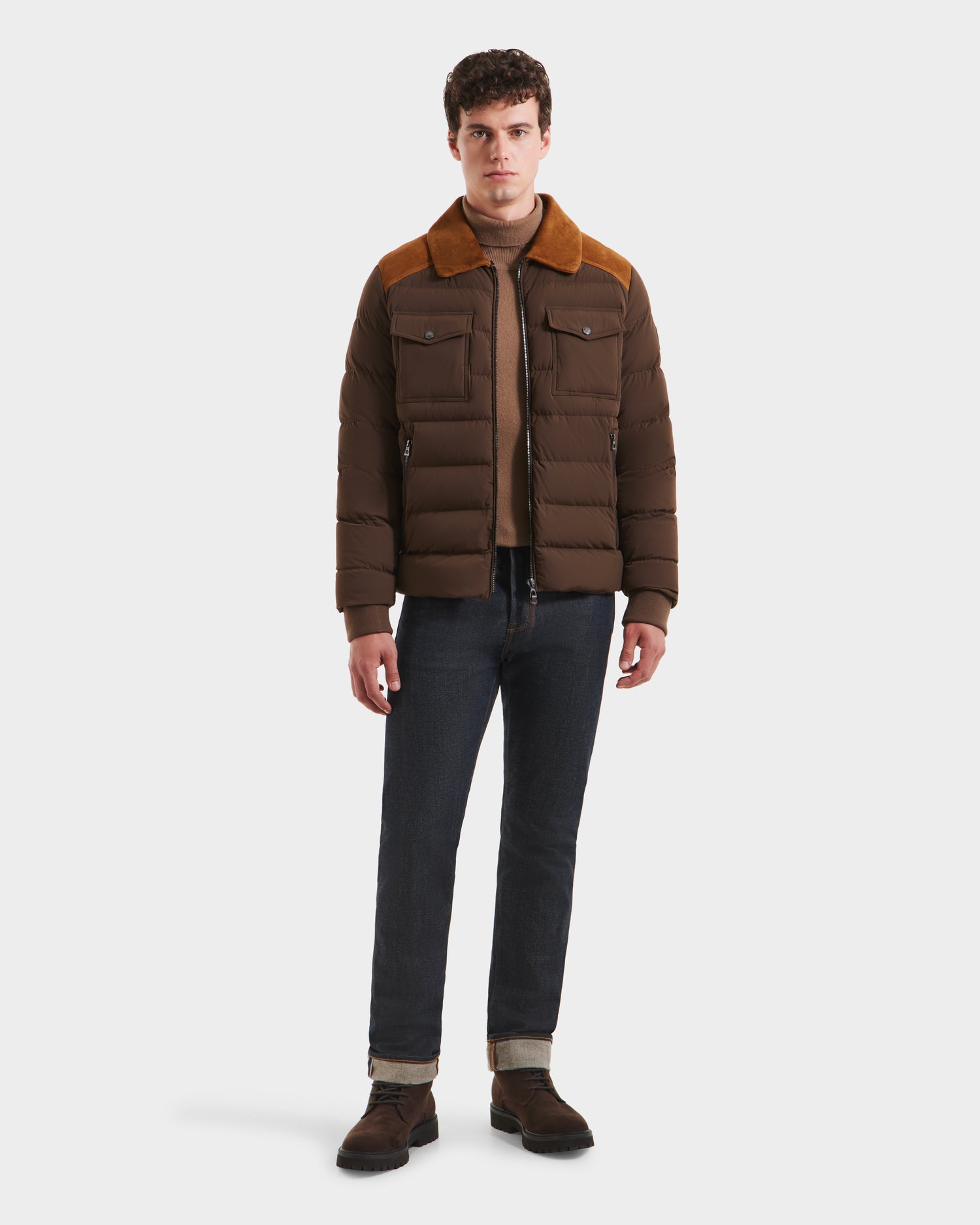 A man faces forward, wearing the Rudsak ANTHONY - 6125042 Mocha brown quilted jacket with a shearling collar over a tan sweater, dark jeans, and brown boots against a plain white background.