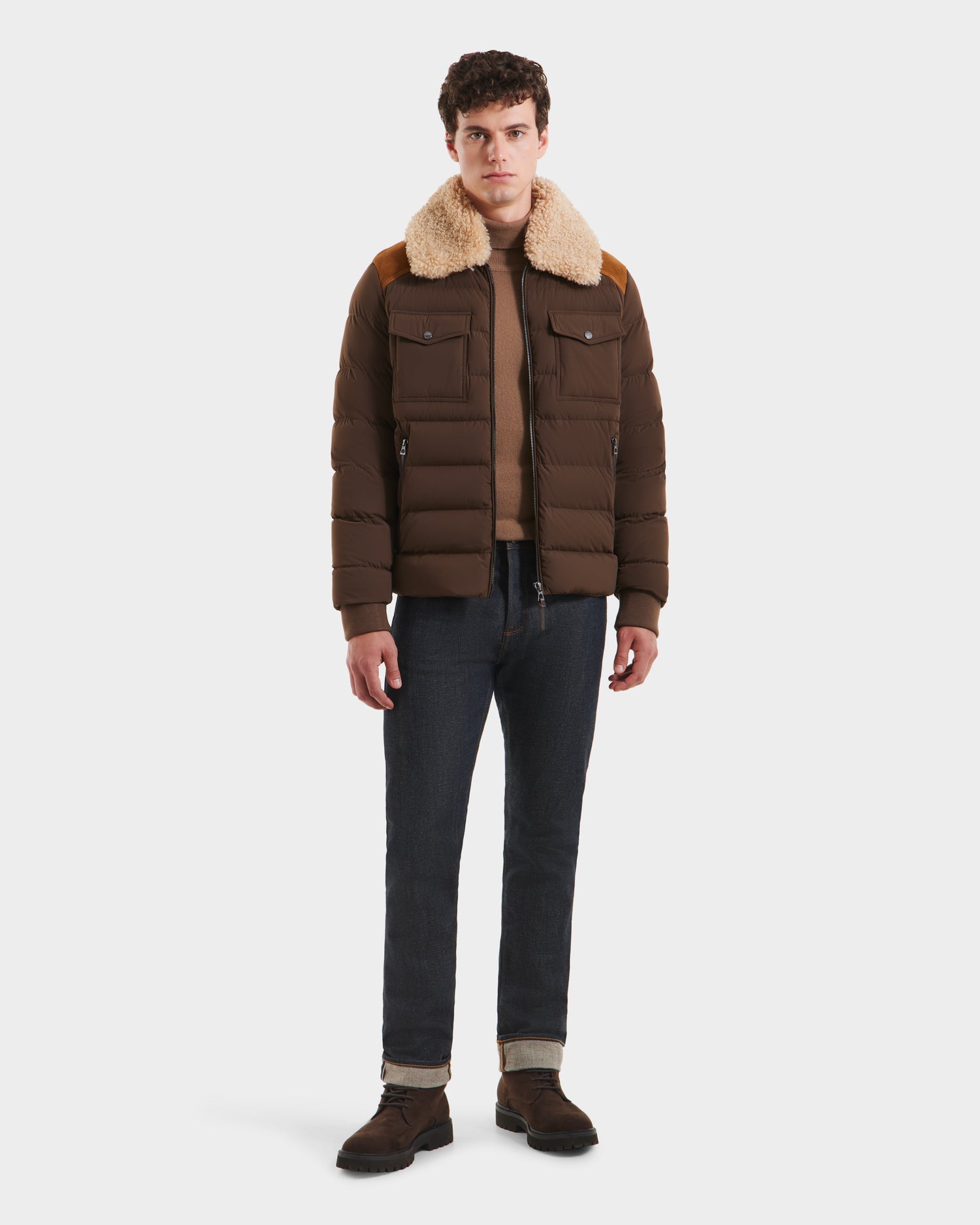 A person stands facing forward, wearing the Rudsak ANTHONY - 6125042 Mocha mens aviator jacket with a tan shearling collar, brown shirt, dark jeans, and dark brown shoes against a plain white background.