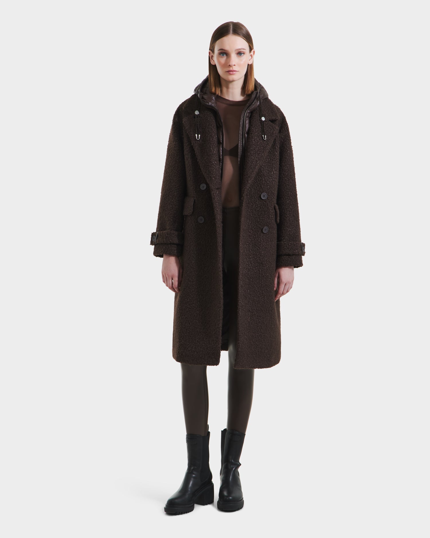 A woman stands facing forward, wearing the Rudsak ARABELLA - 8125621 Espresso long women’s overcoat with rich texture, black leggings, and black ankle boots against a plain white background.