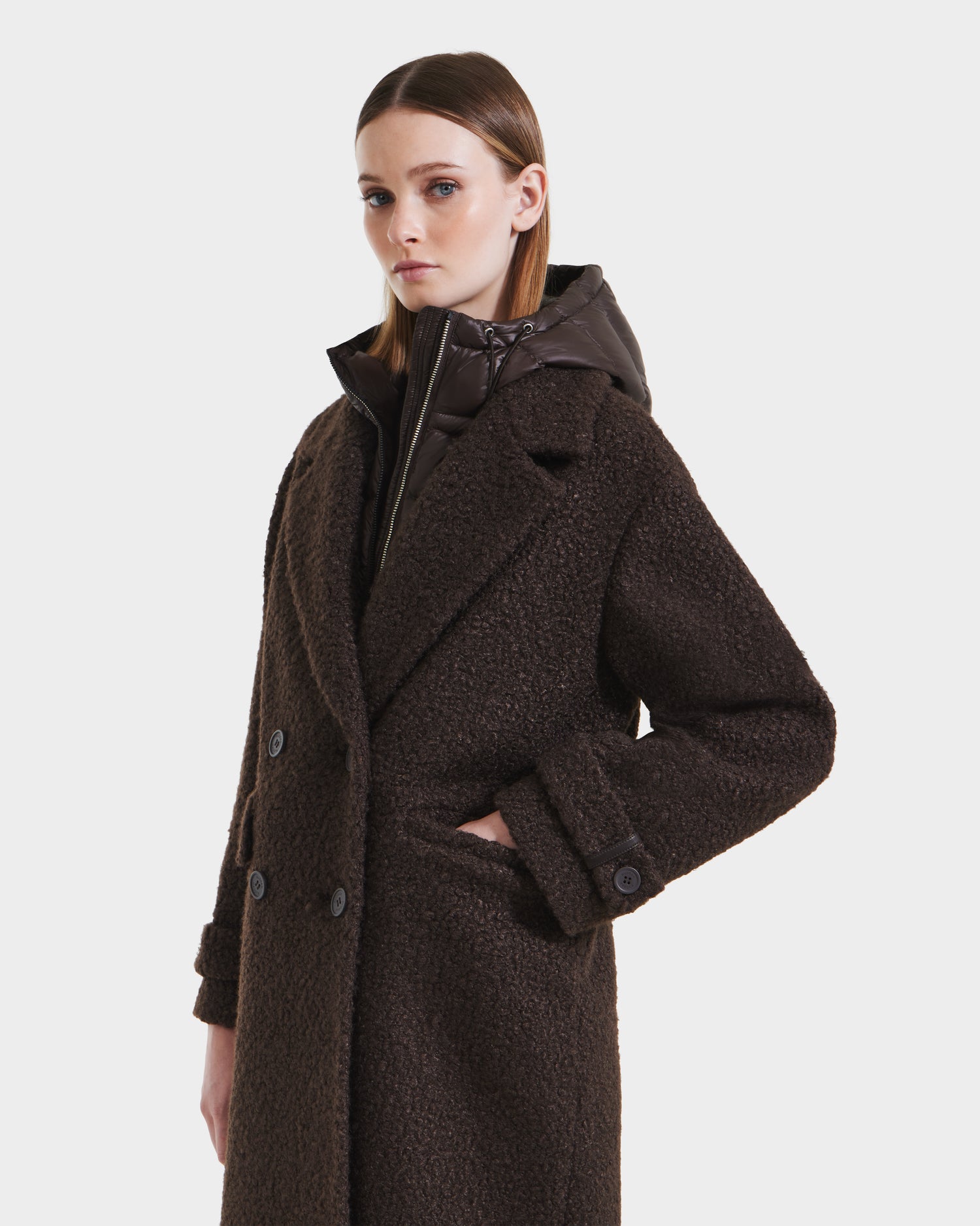 A woman models the Rudsak ARABELLA - 8125621 Espresso overcoat, featuring large lapels and a high-collared inner layer, with one hand in her pocket against a white background.