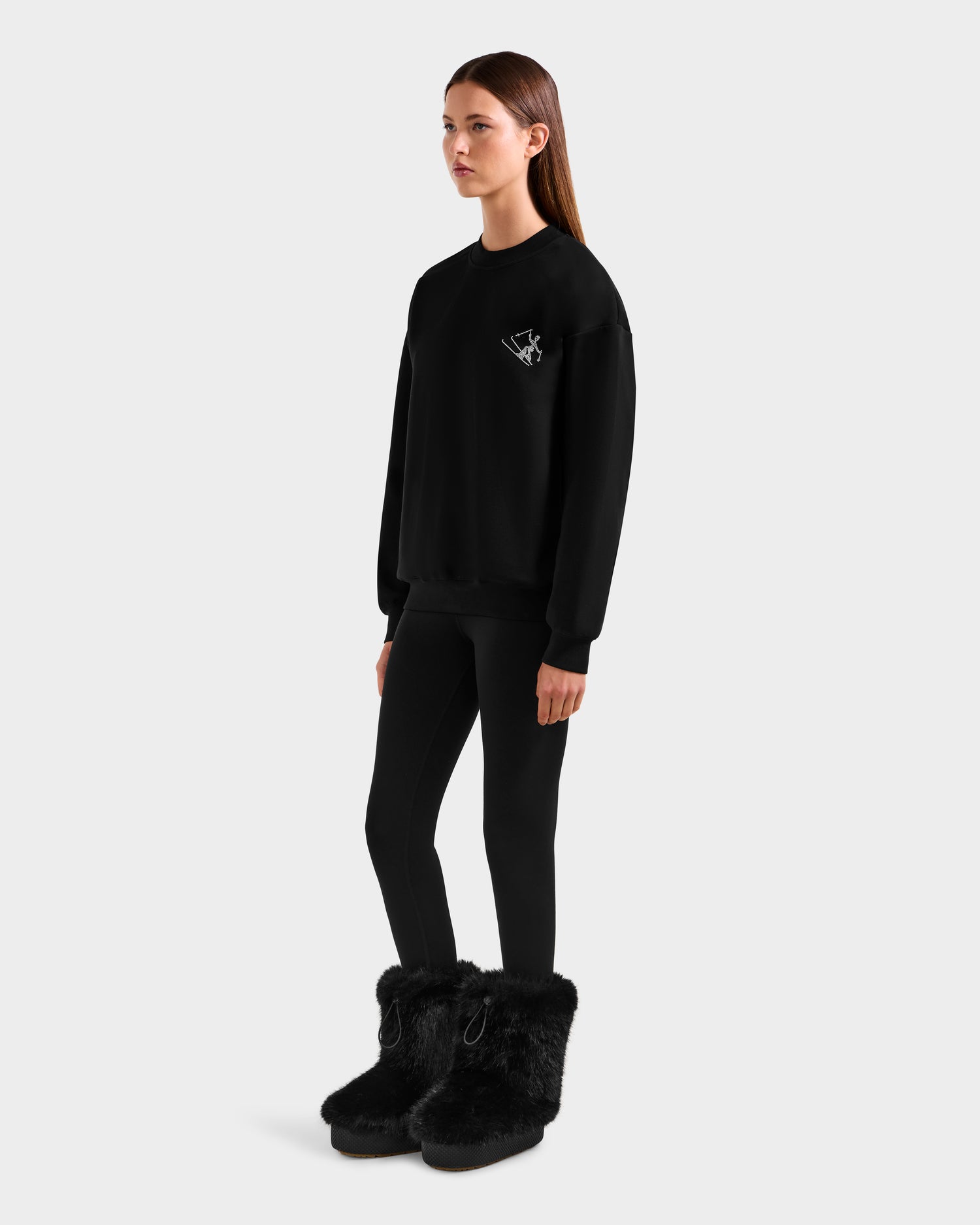 A woman with long straight hair and a neutral expression models the Rudsak ARIA - 8525661 Black crewneck sweatshirt, black leggings, and large furry boots against a plain background in a cozy winter loungewear look, side-facing.