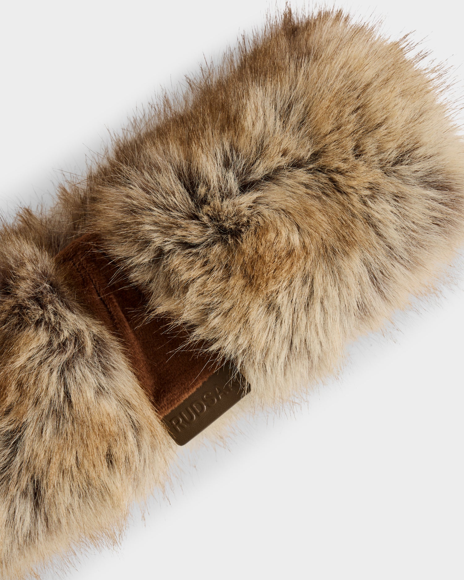 A close-up of the Rudsak ARLETTE - 8425544 Mix Mocha, a soft women’s faux fur headband in brown with a suede patch and embossed text, set against a plain light background.