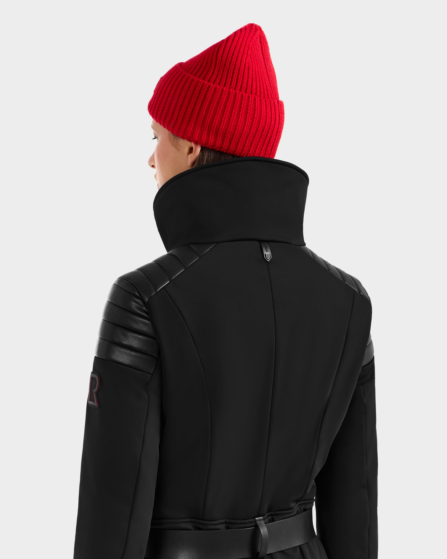 Someone wearing a bright red knit beanie and the Rudsak ARLEY - 8124717 Black jacket, featuring quilted leather details and ski suit-inspired design, is shown from the back against a plain light background.