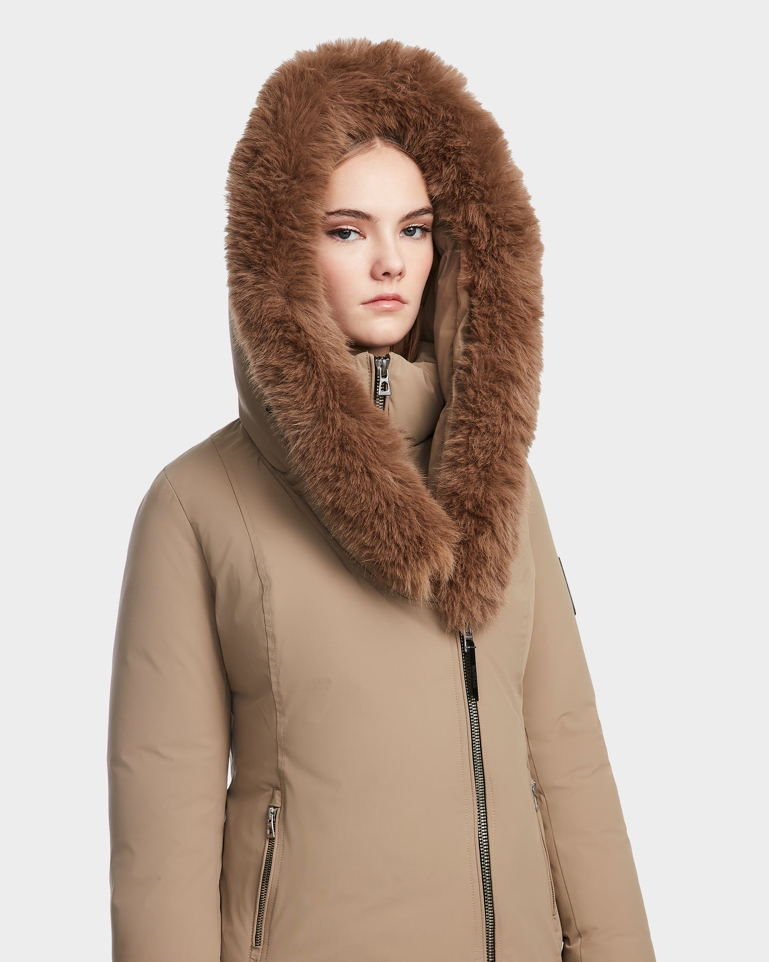 A woman wears the Rudsak AURORE - L123561 Sand fitted down parka with a large brown faux fur hood, looking forward with a neutral expression against a plain white background.