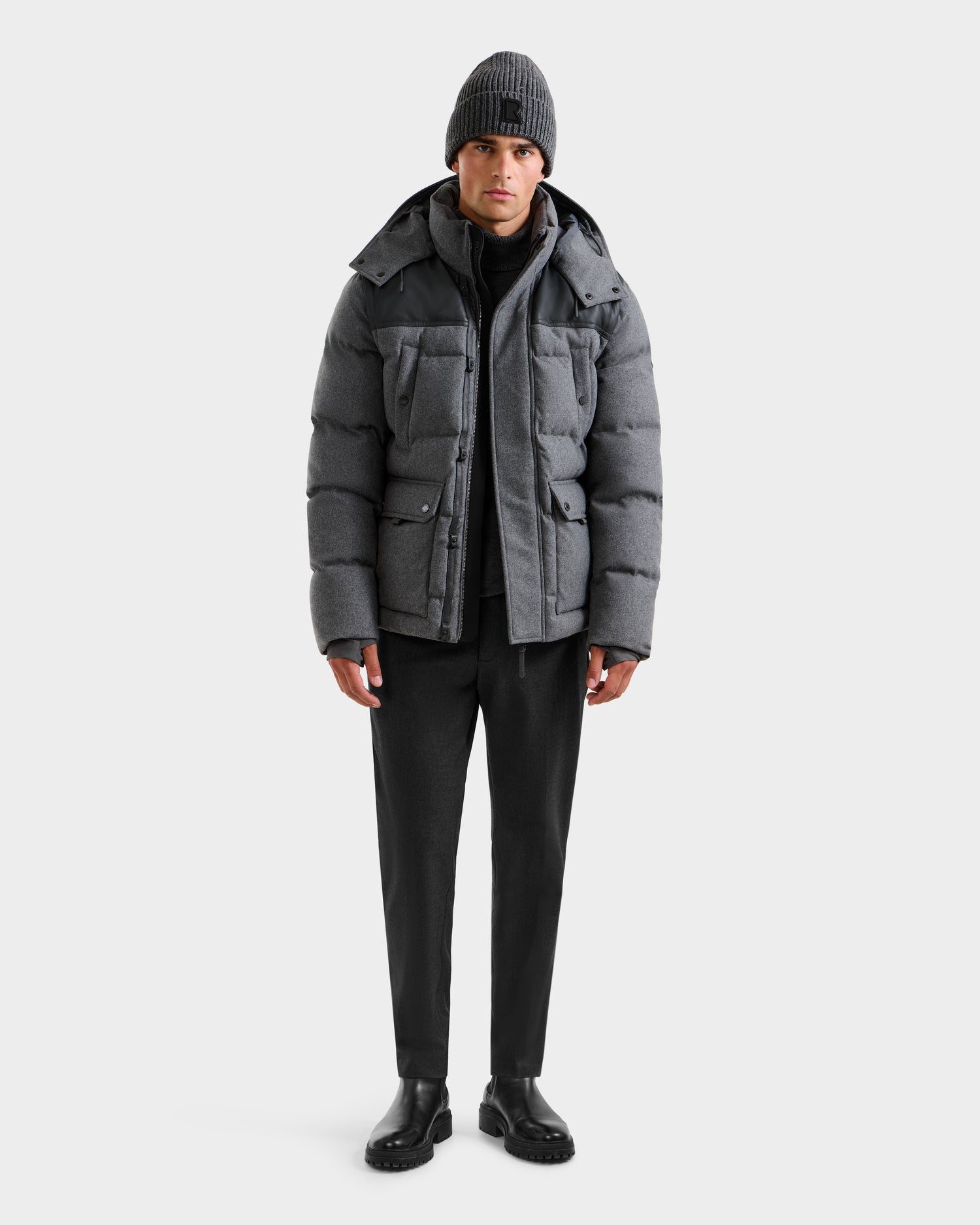 A person wearing the Rudsak BALDWIN W - 6125532 Heather Charcoal parka stands facing forward against a plain white background, styled with black pants, black boots, and a gray knit beanie.