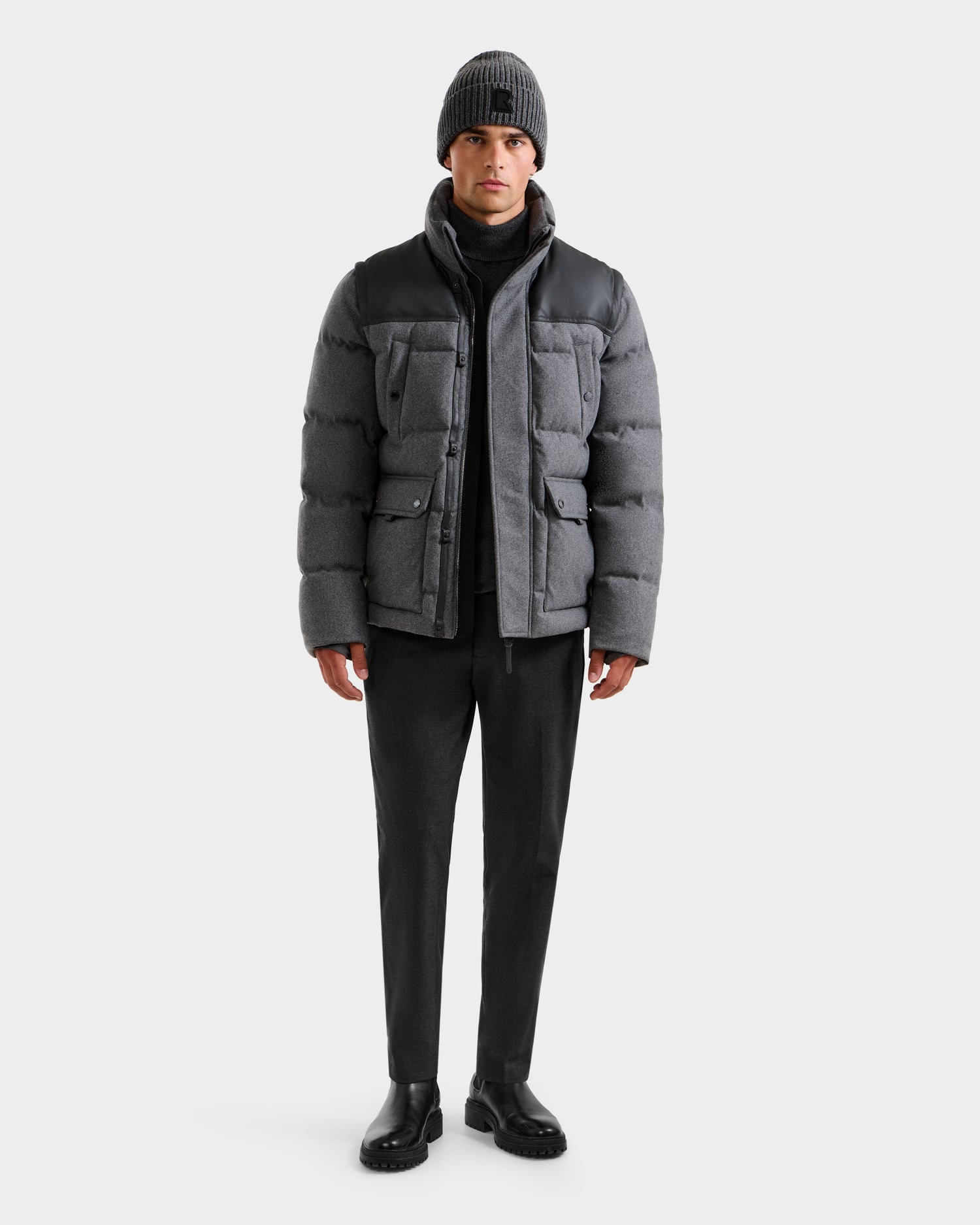 A man wears the BALDWIN W - 6125532 Heather Charcoal parka by Rudsak, styled with black pants, shoes, and a gray knit beanie as he stands facing forward against a plain light background for a timeless winter look.